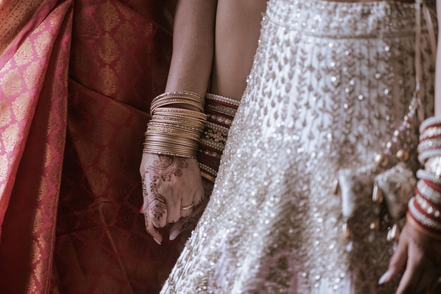 Close-up of Indian bride and mother holding hands in traditional embroidered wedding attire.