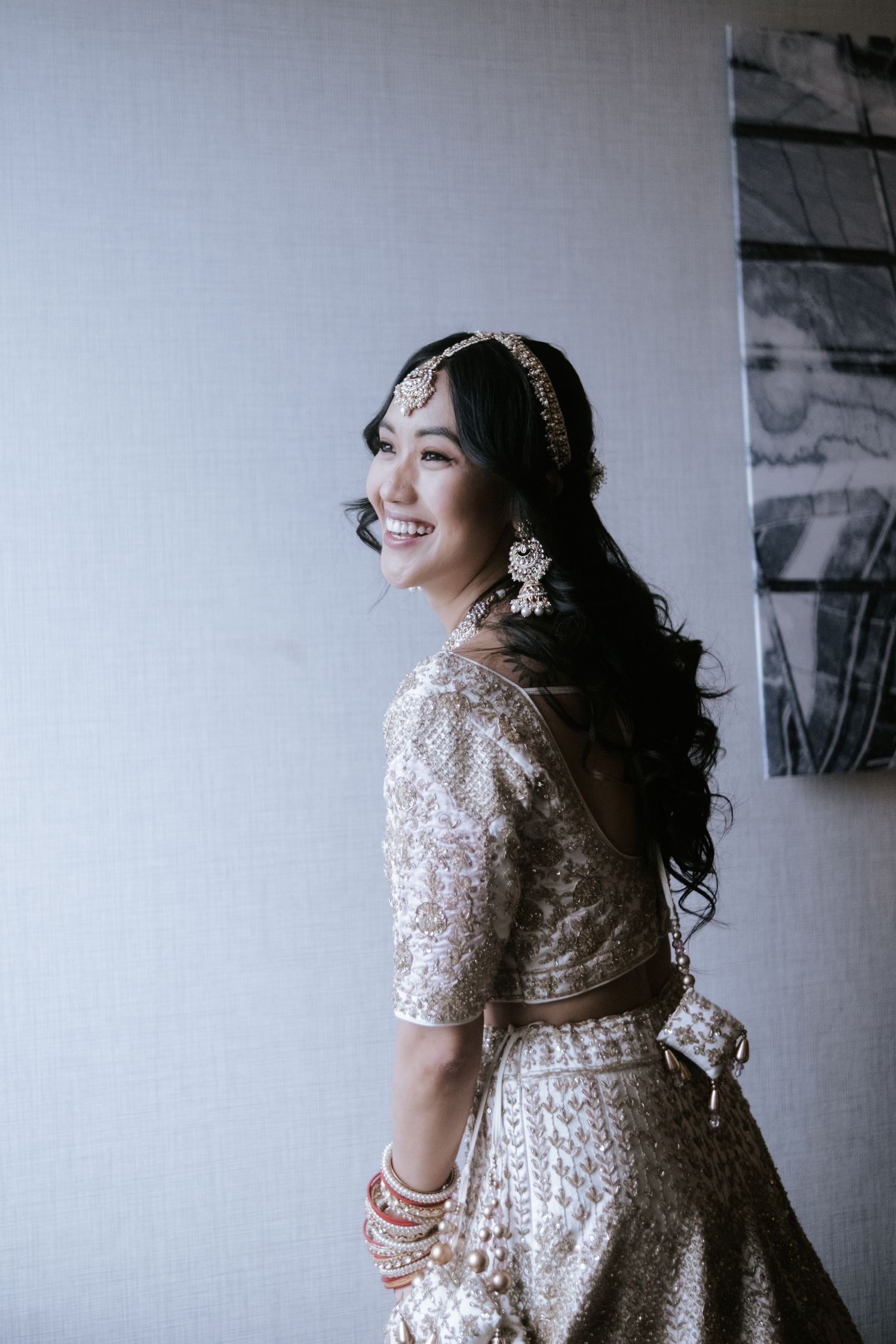 Smiling Indian bride in gold embroidered lehenga with bridal jewelry poses elegantly.