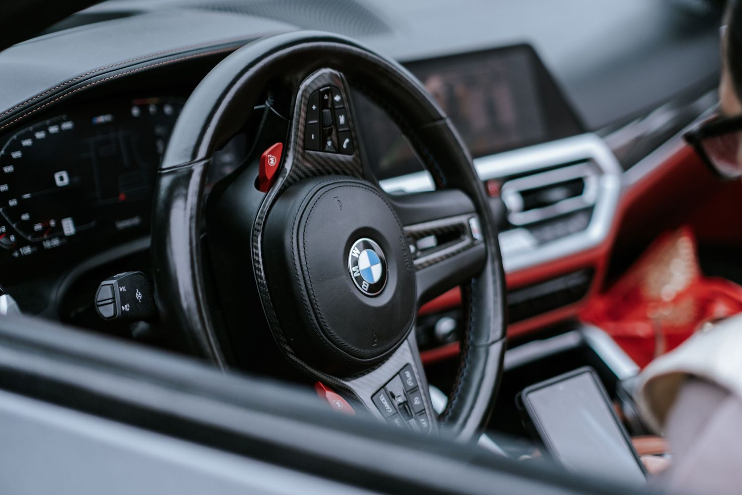 Close-up of a BMW steering wheel with blue logo and red accents in a luxury car interior.