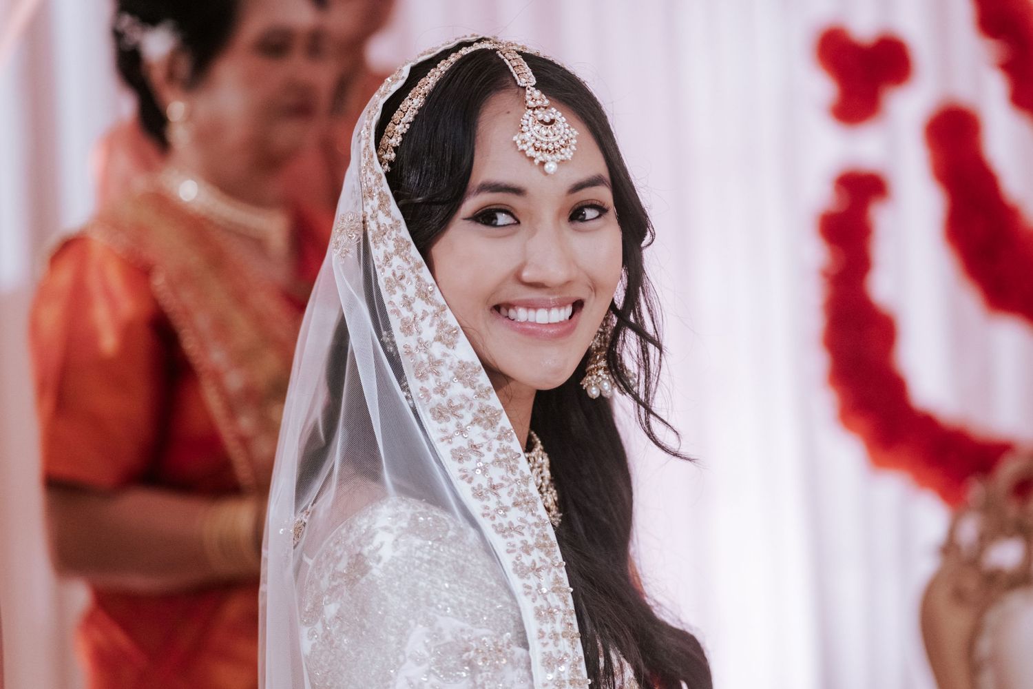 Beautiful bride smiling in white bridal lehenga with maang tikka and veil at Hindu wedding.