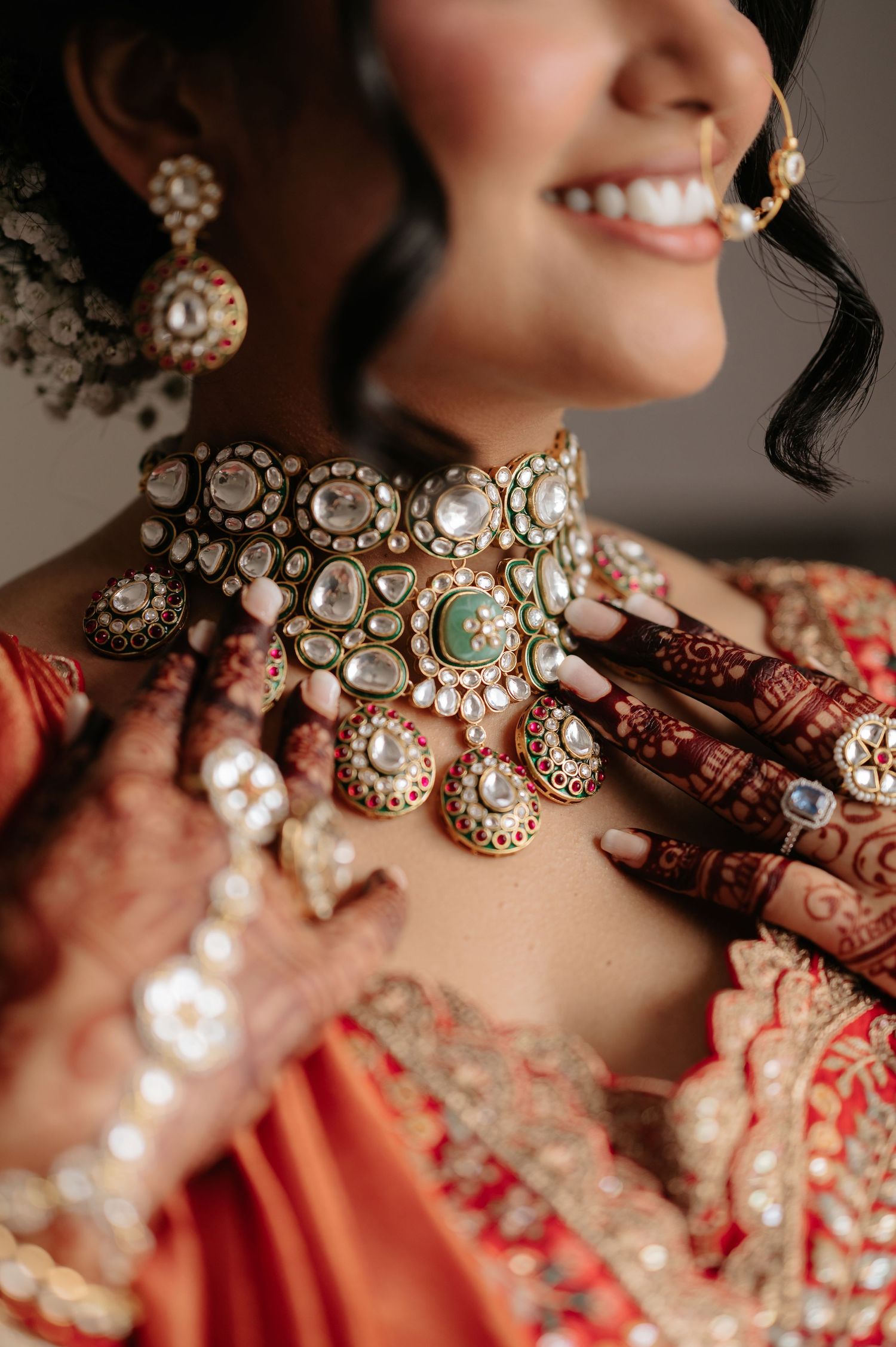 Close-up of Indian bride wearing ornate kundan choker necklace with intricate mehndi on hands.