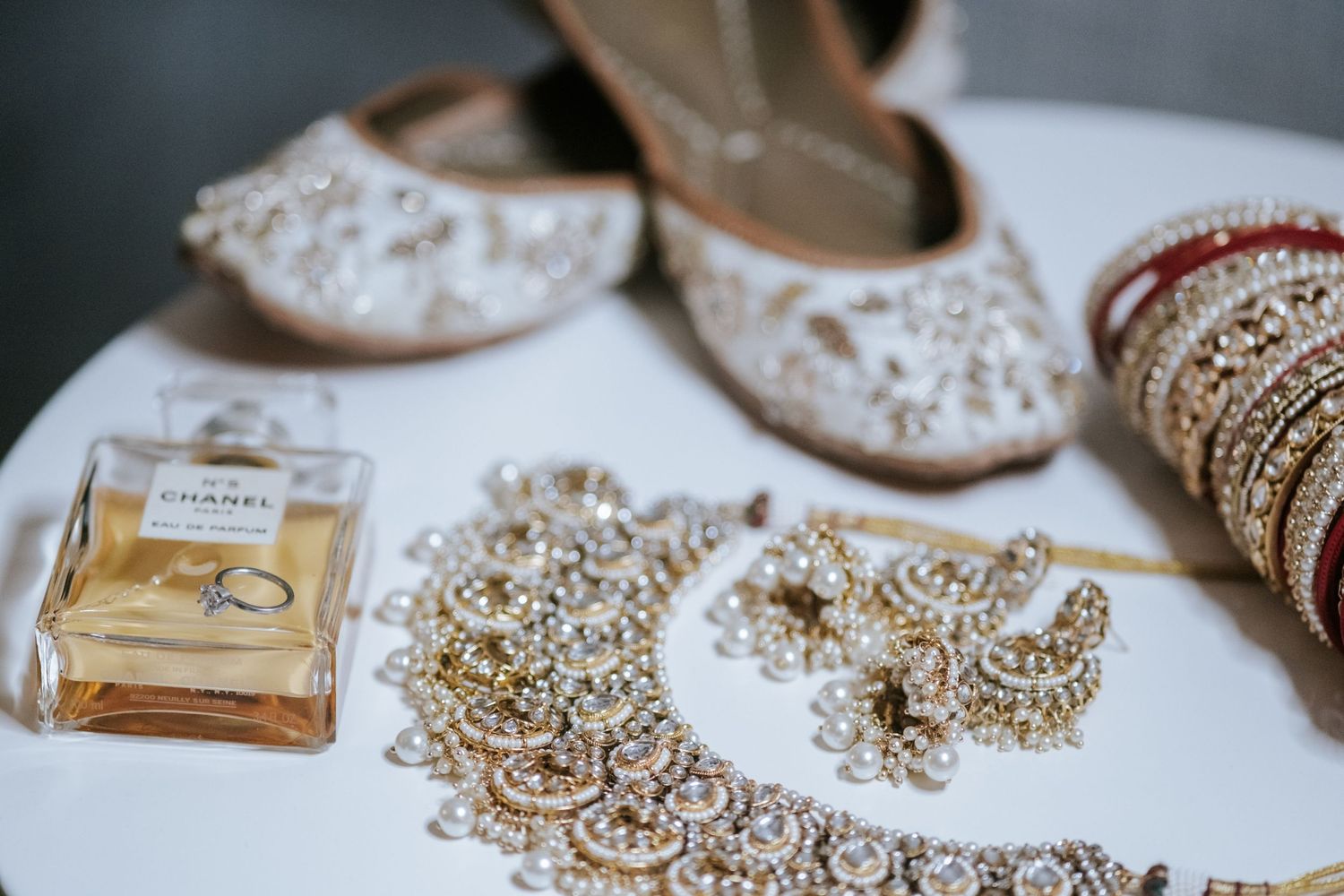 Indian bridal accessories including embellished shoes, gold jewelry, bangles, and Chanel perfume.