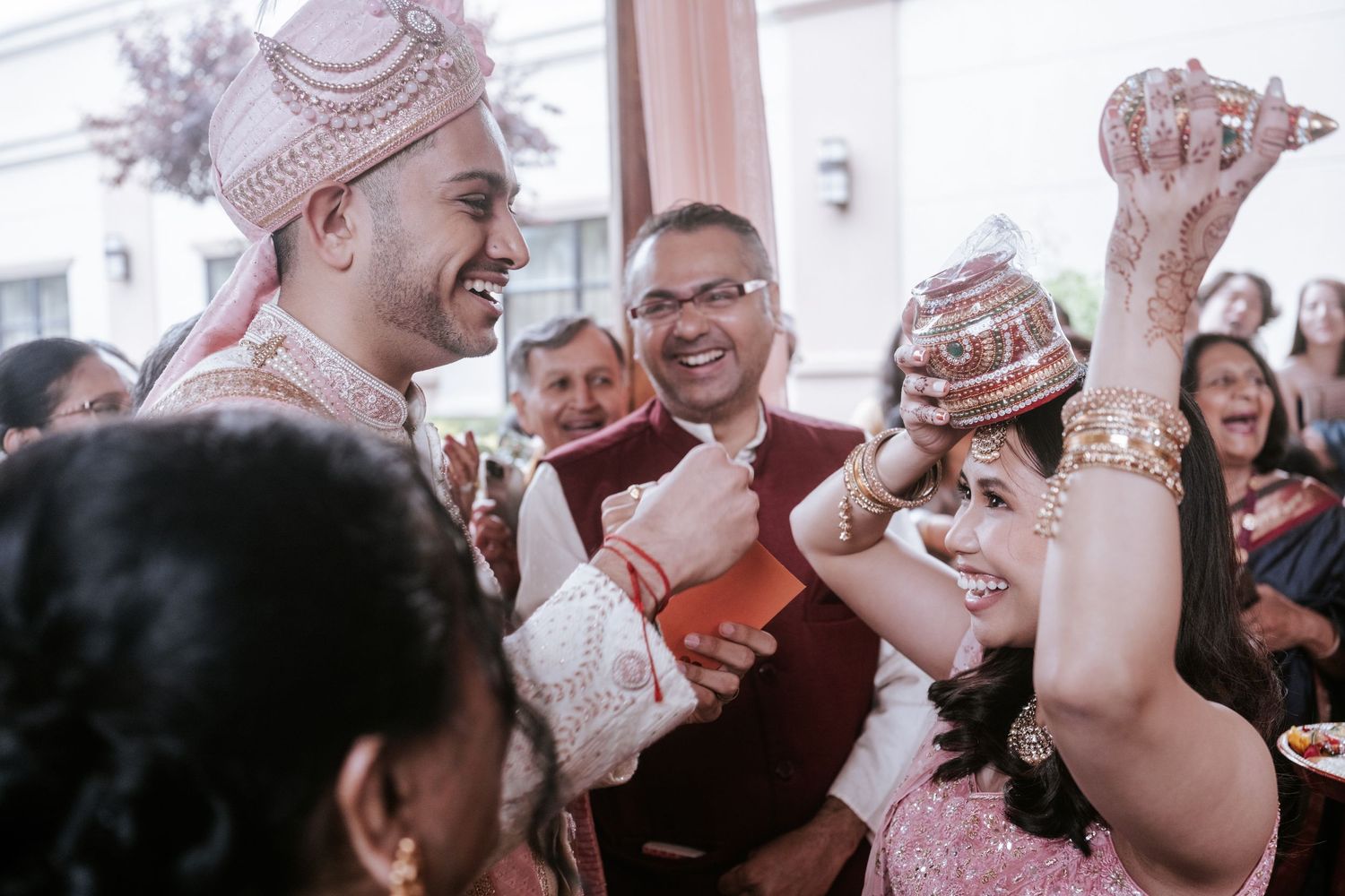 Indian groom in pink sherwani laughs during traditional wedding ceremony greeting with bride.