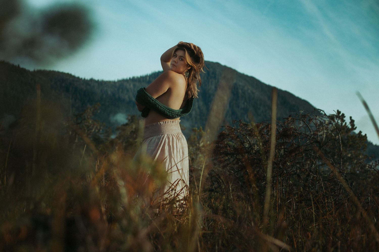 A person in a flowy white dress stands gracefully in front of a mountain landscape at sunset.