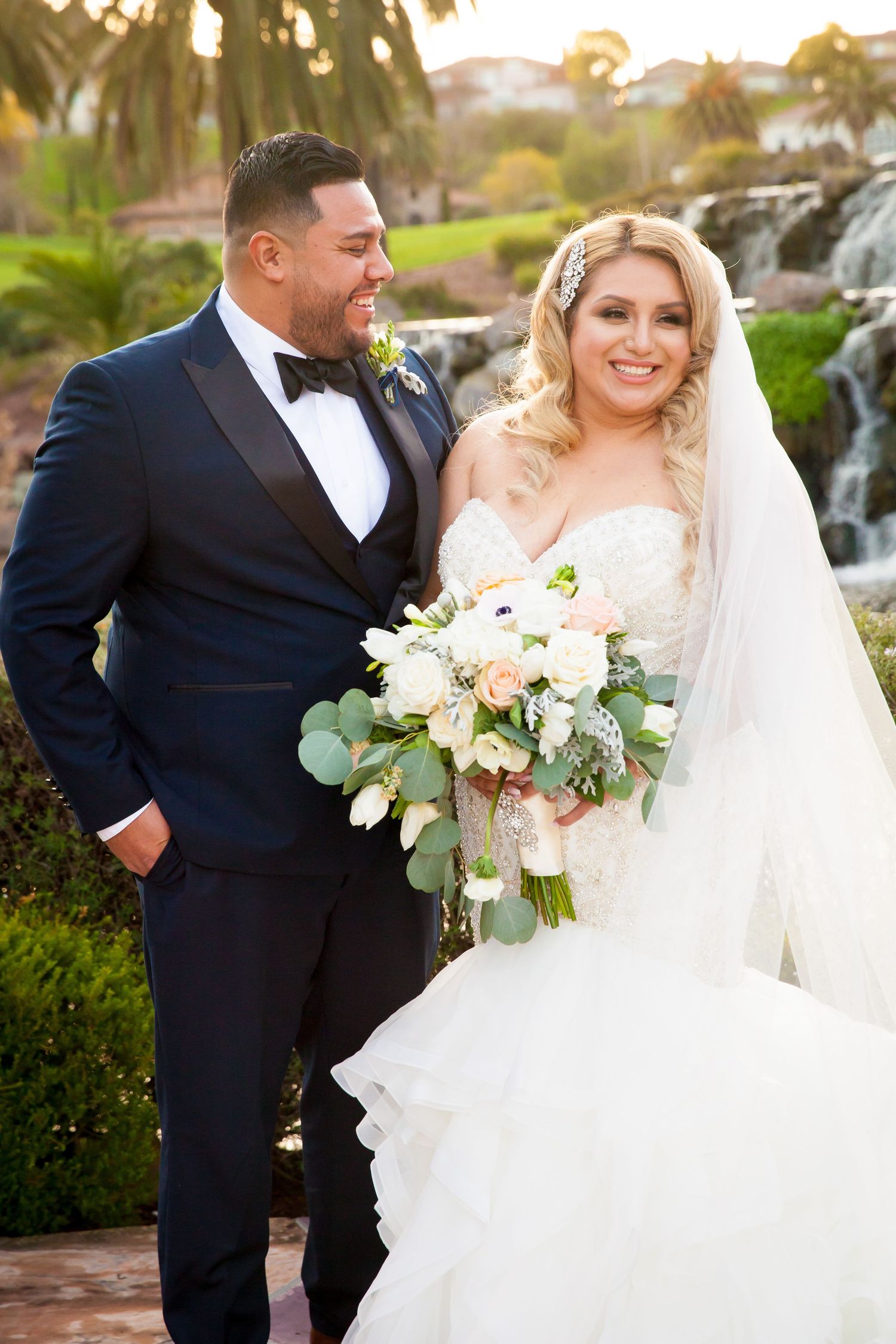 Newlywed couple shares joyful moments together outdoors near a waterfall on their wedding day.
