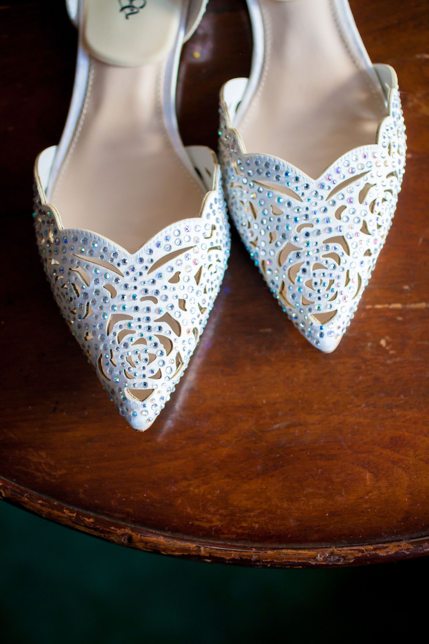 Close-up view of elegant white lace bridal shoes with intricate cutout details on a wooden surface.
