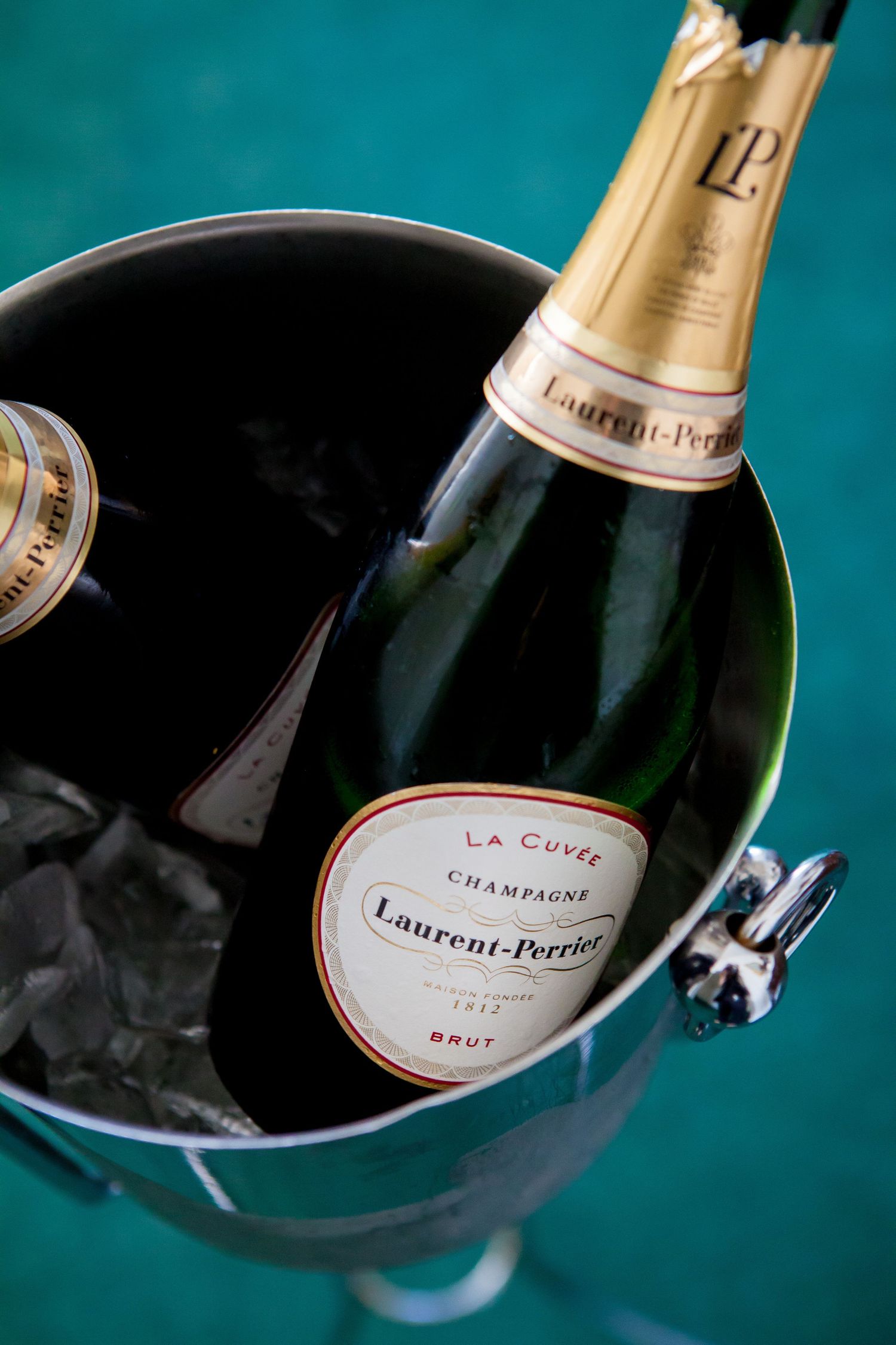 A series of champagne bottles and glasses arranged artistically against a dark teal background with dramatic lighting.