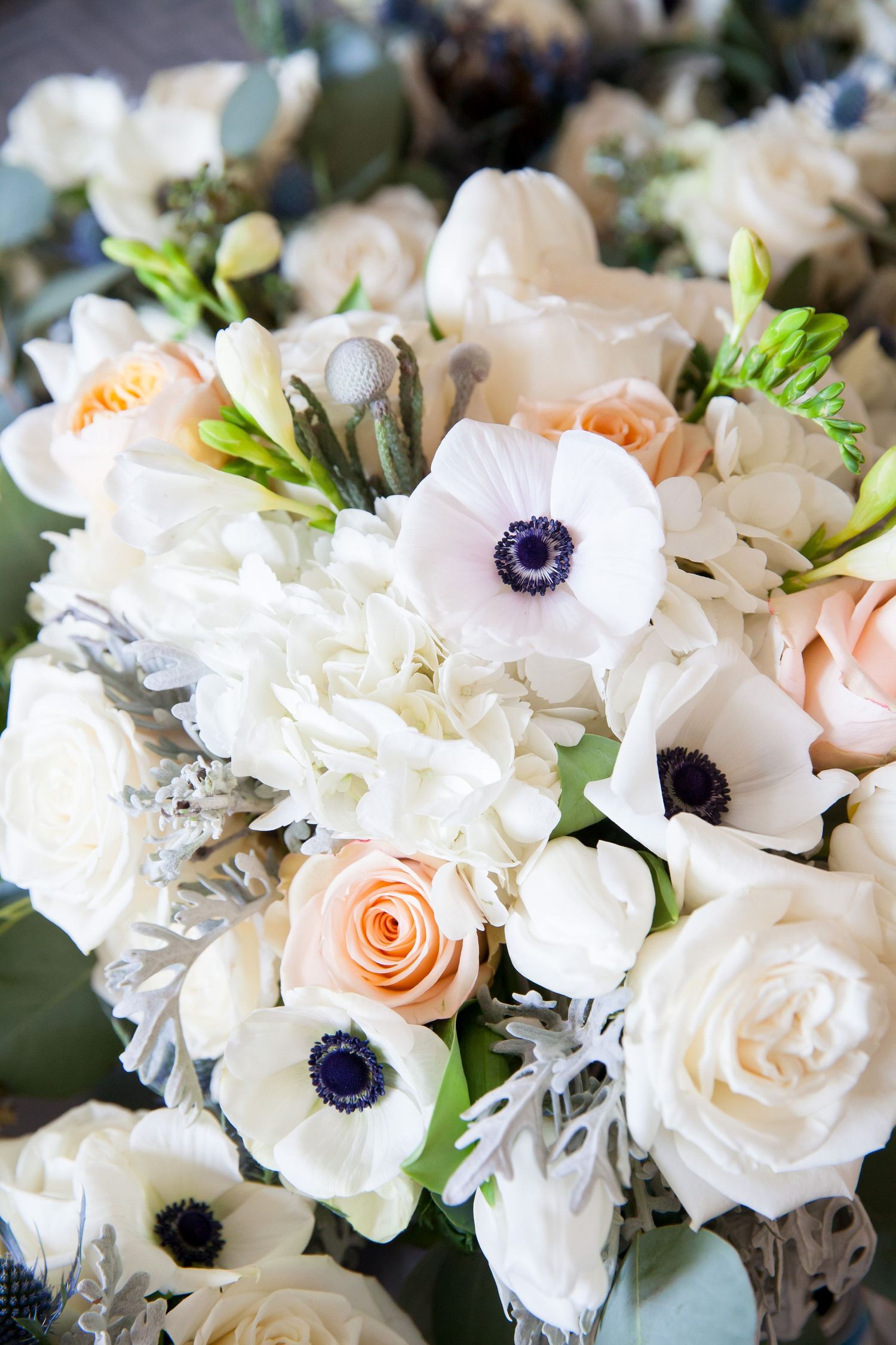 A romantic floral arrangement featuring white anemones, peach roses, and white carnations in a soft, elegant design.
