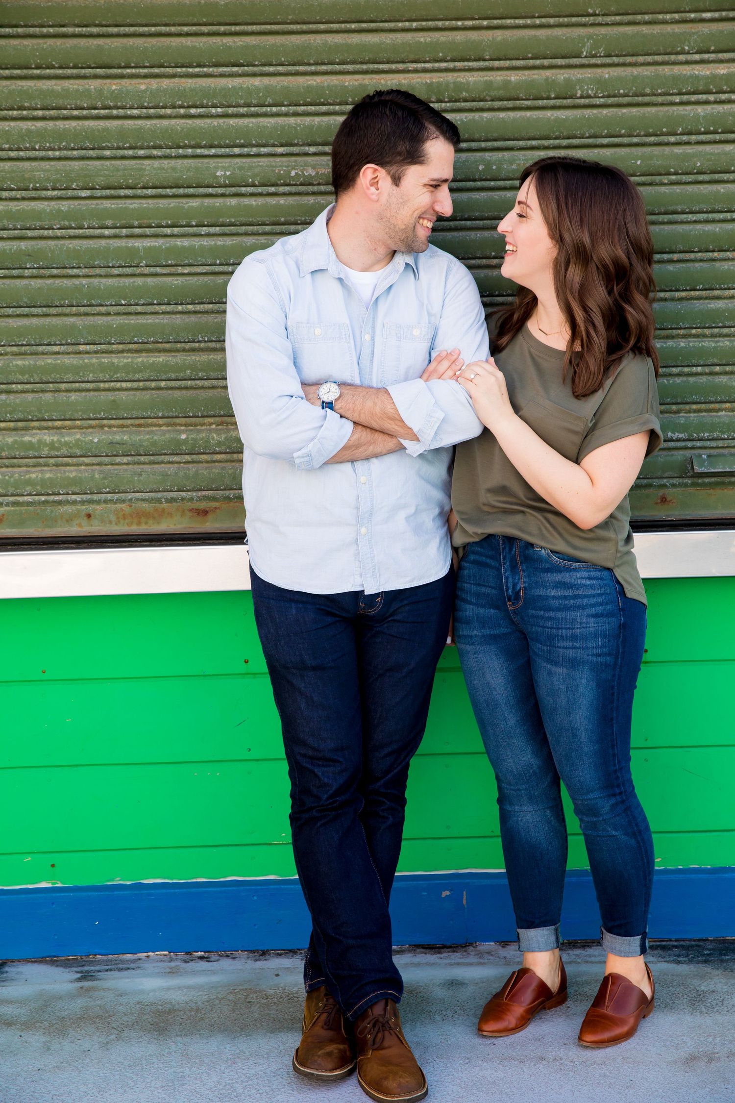 A couple in casual attire leans against a striped wall, creating a series of playful romantic poses together.