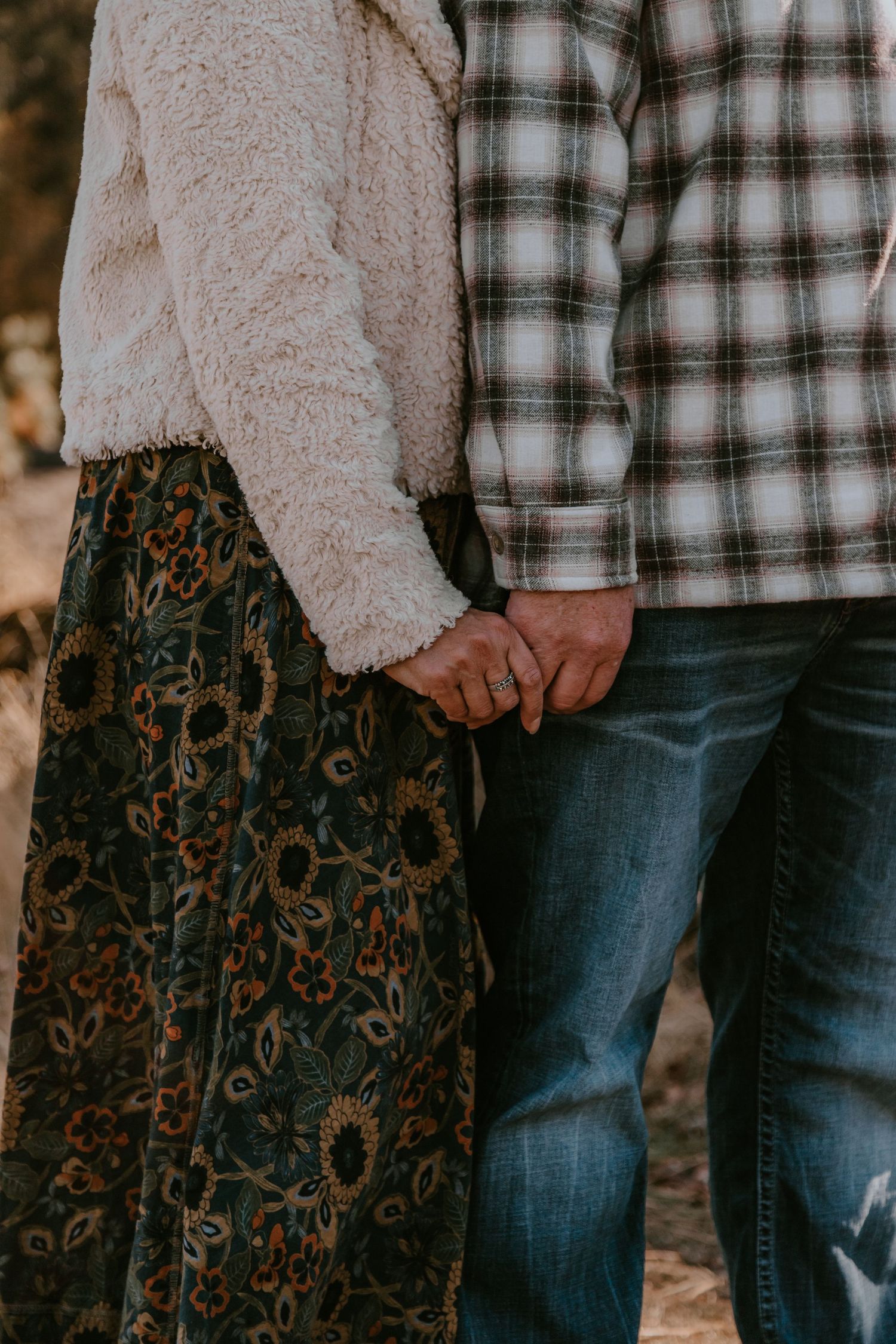 Close-up view of two people standing together wearing a plaid shirt, fuzzy sweater and jeans in an autumn setting.