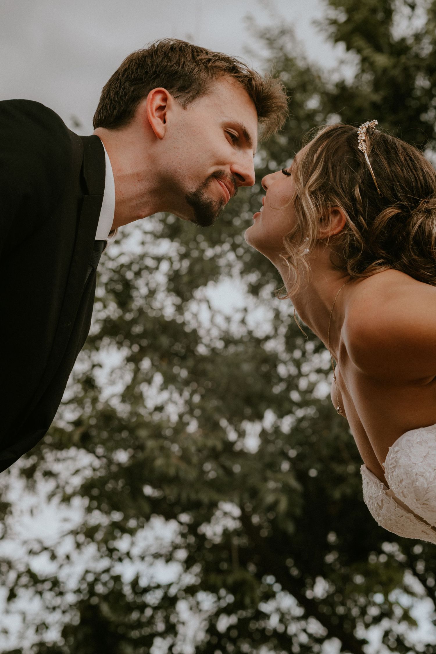 Couple shares intimate moment during golden hour wedding photoshoot with trees in background.