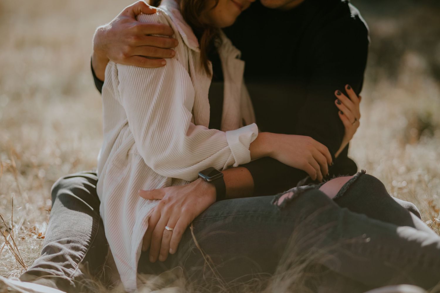 A romantic couple sits close together outdoors surrounded by glowing bokeh lights during a dreamy sunset moment.