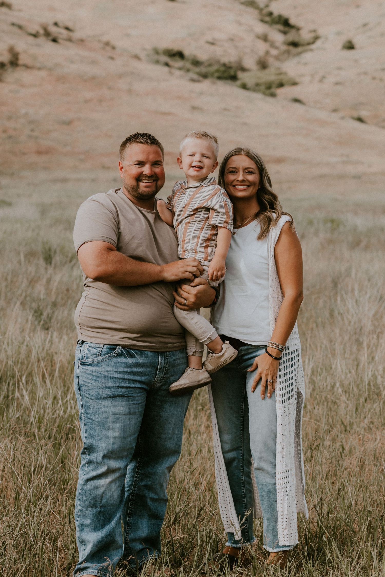 A joyful family embraces and laughs together while standing in a grassy field during golden hour.