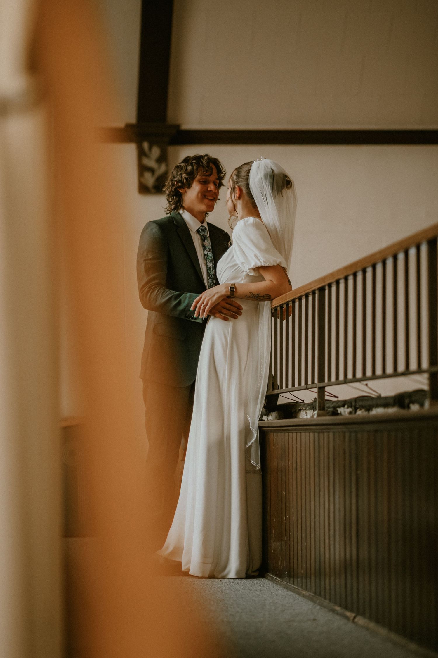 A romantic wedding photo of a couple embracing by a staircase in warm vintage lighting.