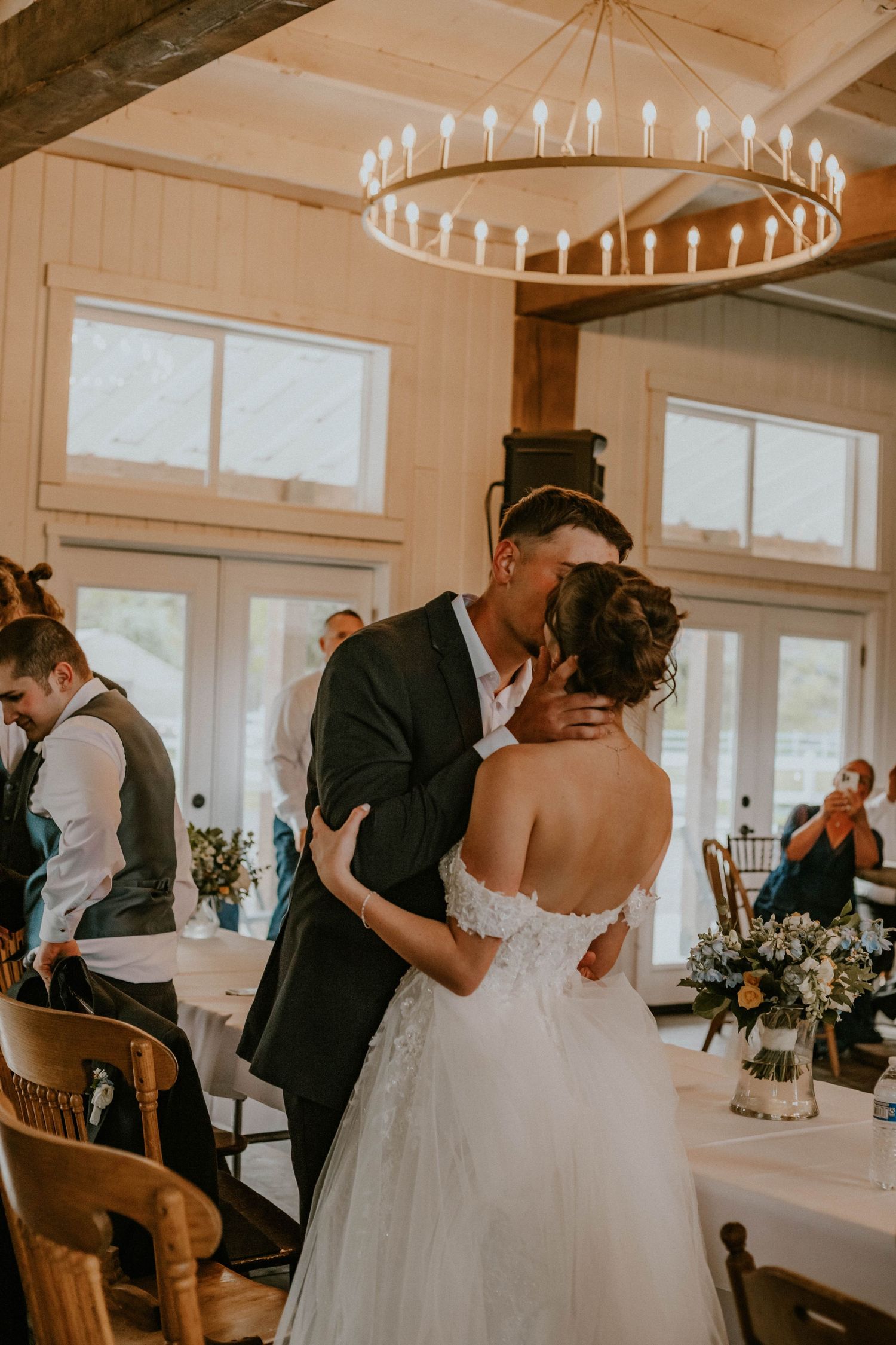 Couple shares an intimate moment during their first dance under a circular candle chandelier at an elegant rustic reception venue.