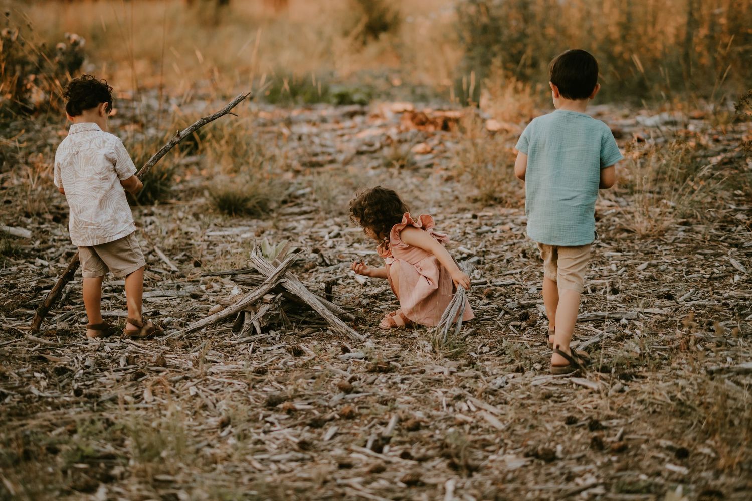 Three young children playing together on rocky terrain during golden hour sunset lighting.