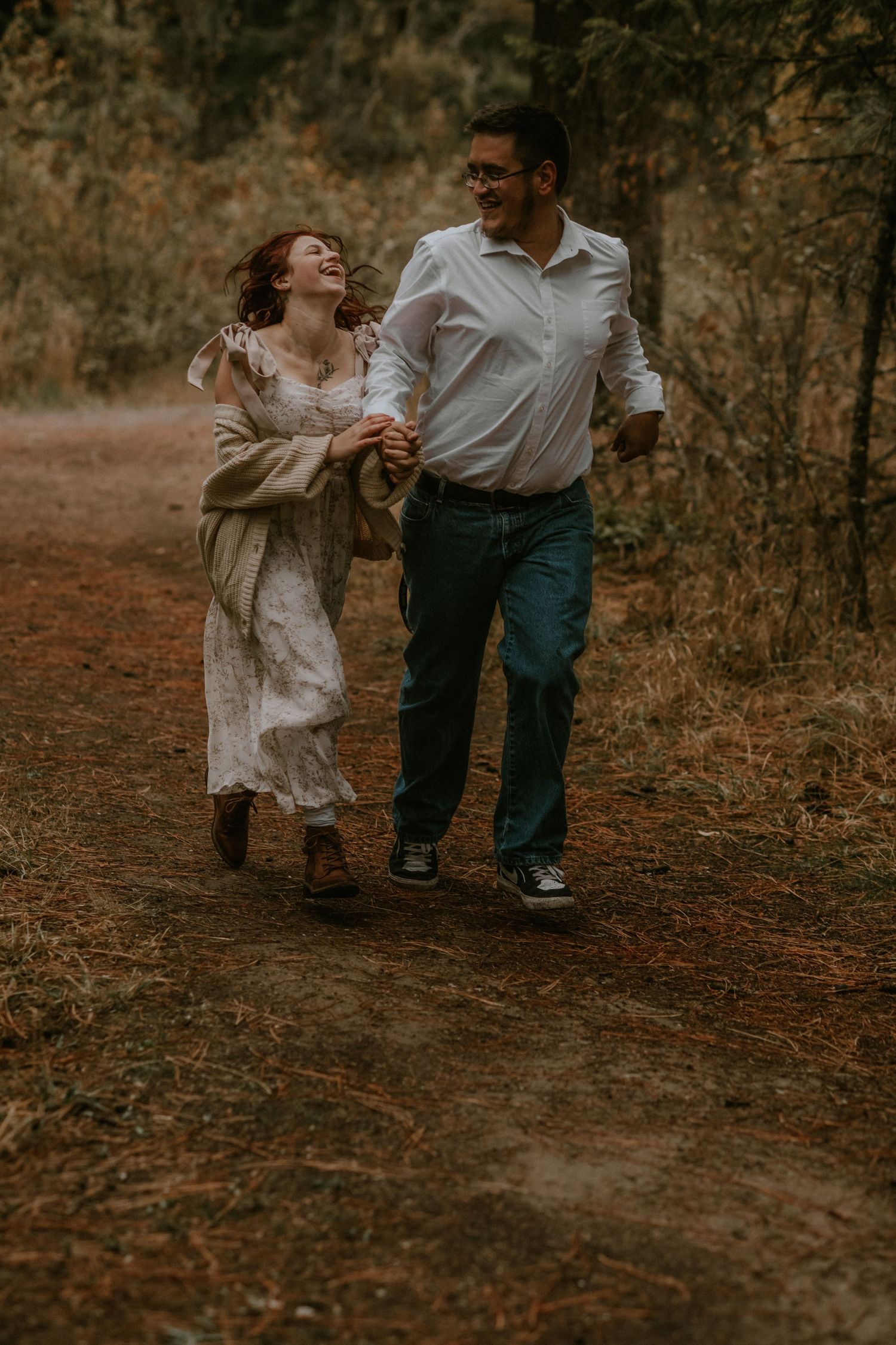 A couple dances together on a forest path during autumn with warm moody lighting and fallen leaves.