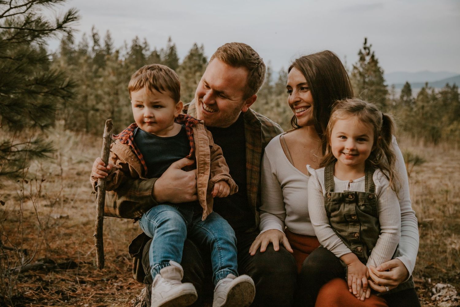 A family enjoys a warm autumn day together outdoors in a natural setting with pine trees in the background.