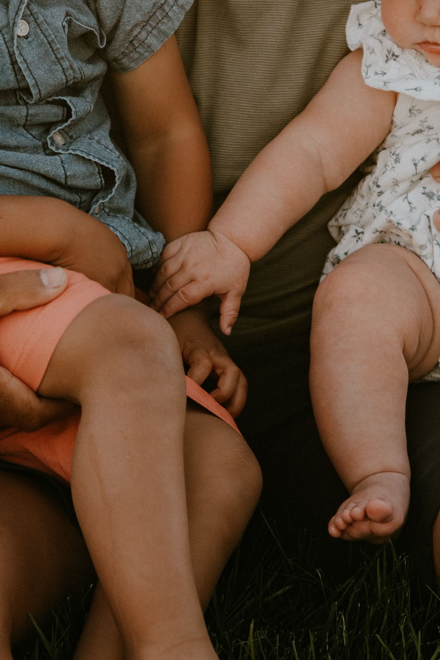 Close-up of children's legs sitting on grass, wearing summer clothing and barefoot.