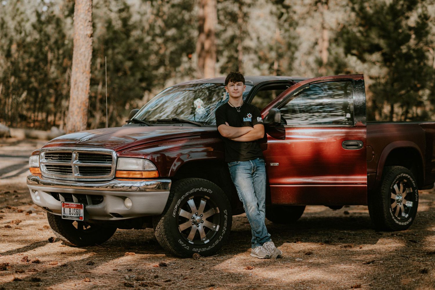 A red Dodge Ram pickup truck parked in a wooded area with pine trees in the background.