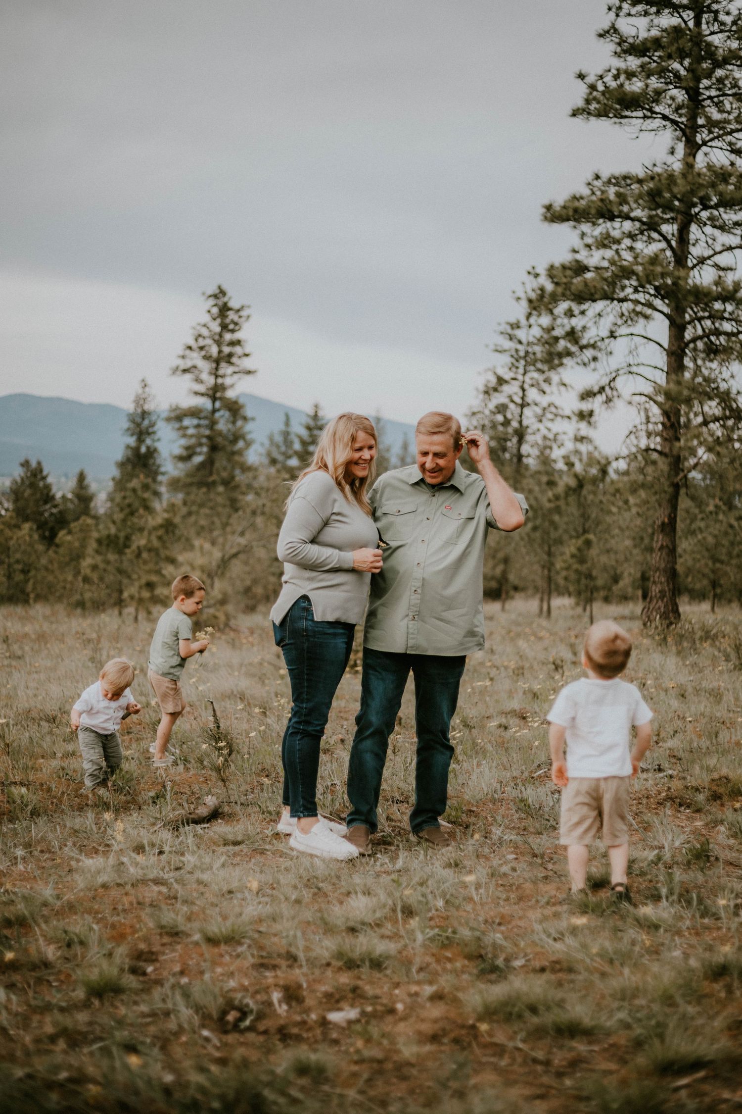Family spending time together in a scenic mountain meadow surrounded by tall pine trees on an overcast day.