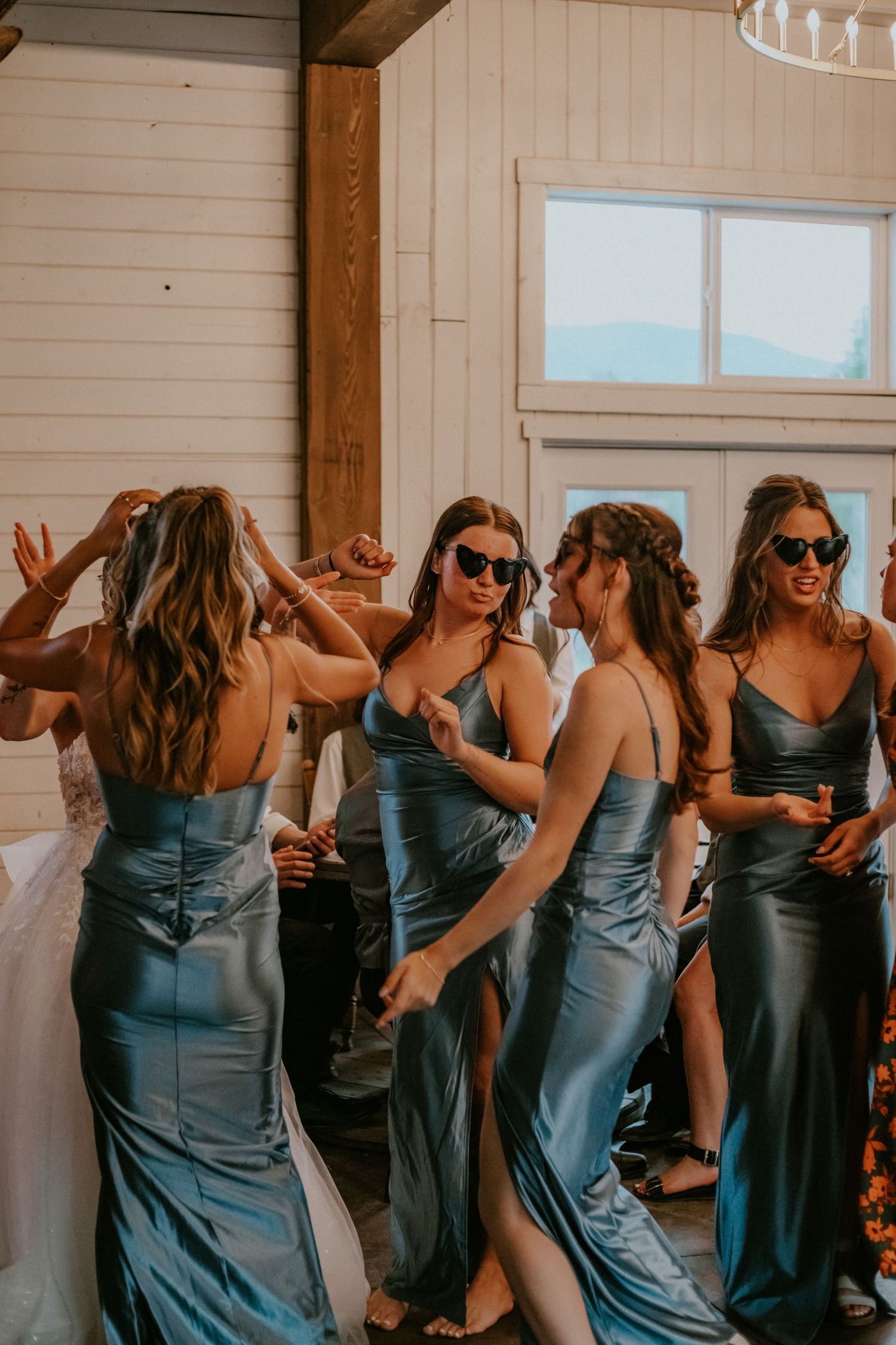 A group of bridesmaids in matching teal satin dresses dance and celebrate together at a wedding reception.