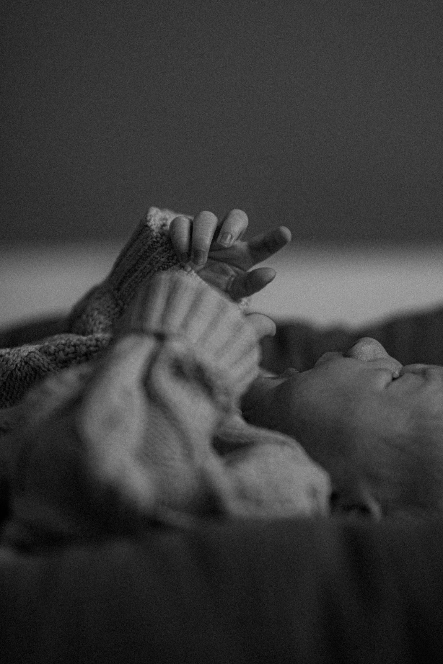 A black and white close-up photo of a baby's hands and face lying down in soft lighting.