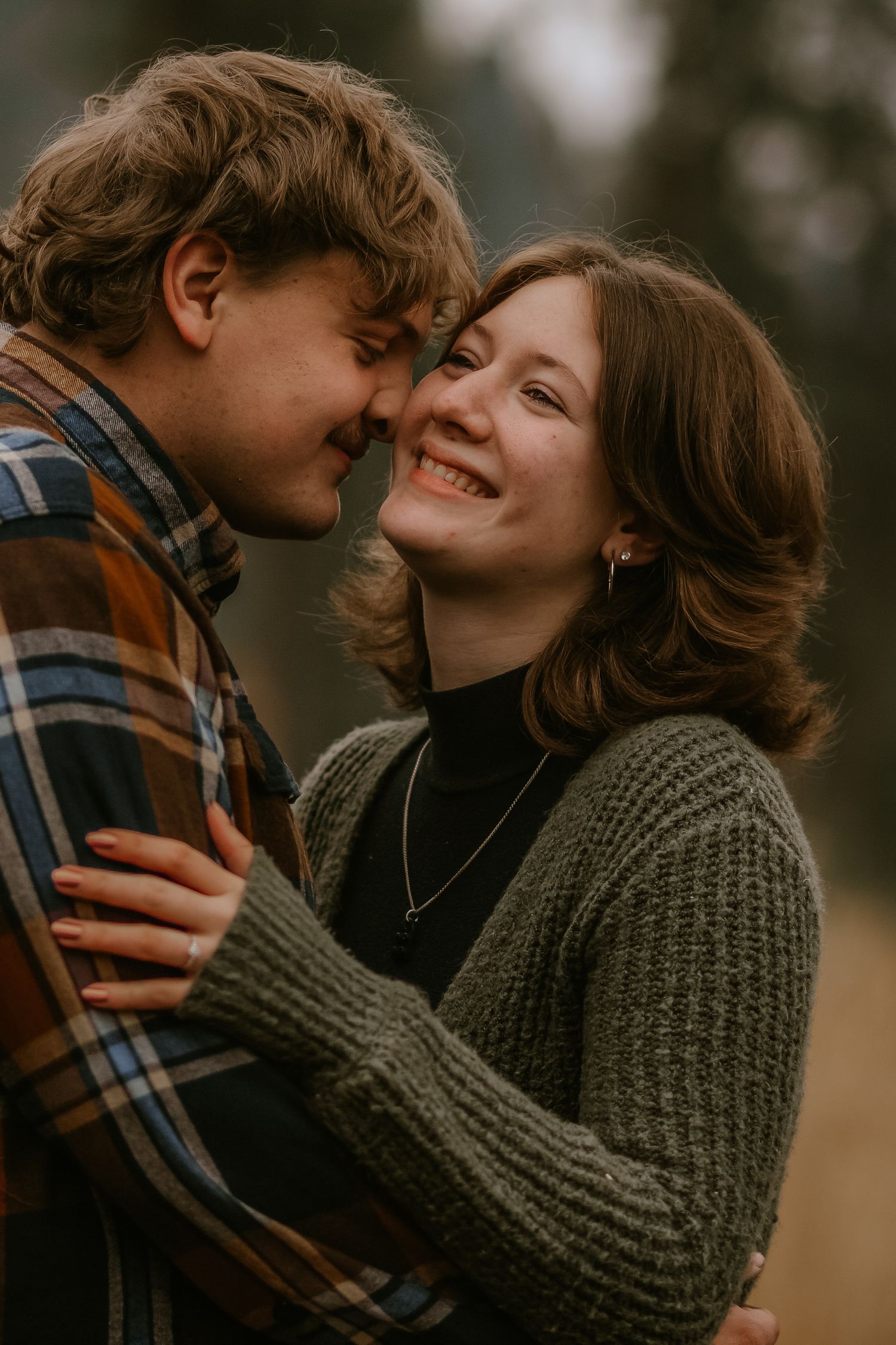 Romantic couple embraces outdoors in warm autumn light, wearing cozy sweaters and sharing intimate moment.