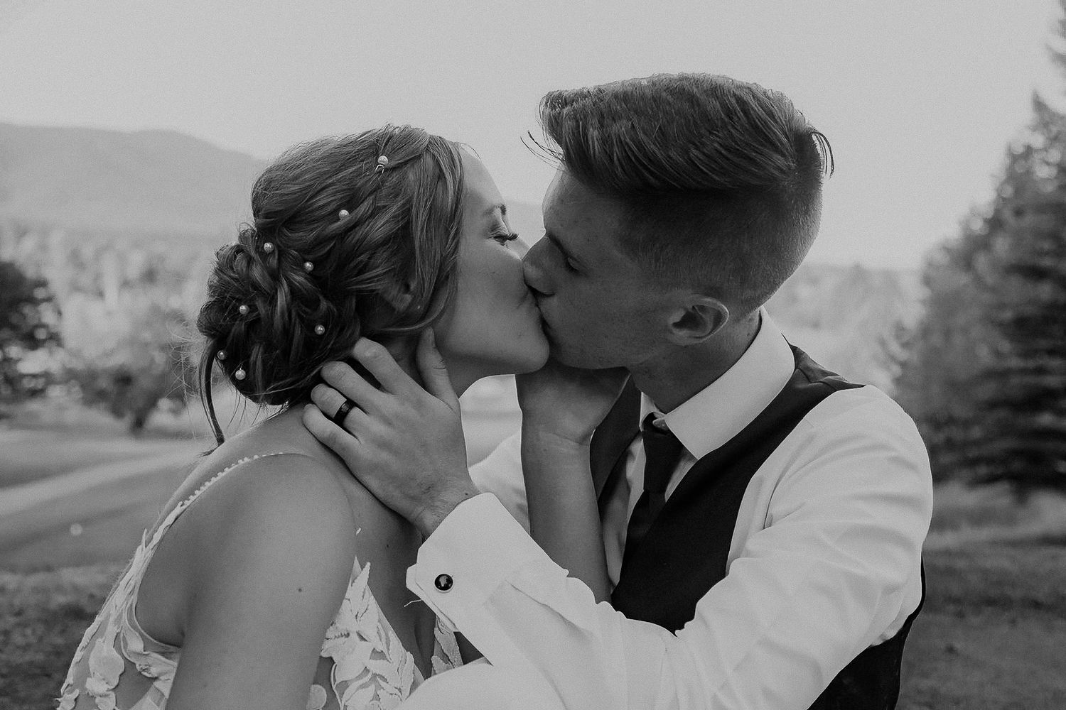A tender kiss shared between a couple in wedding attire on their special day, set against a mountain landscape.