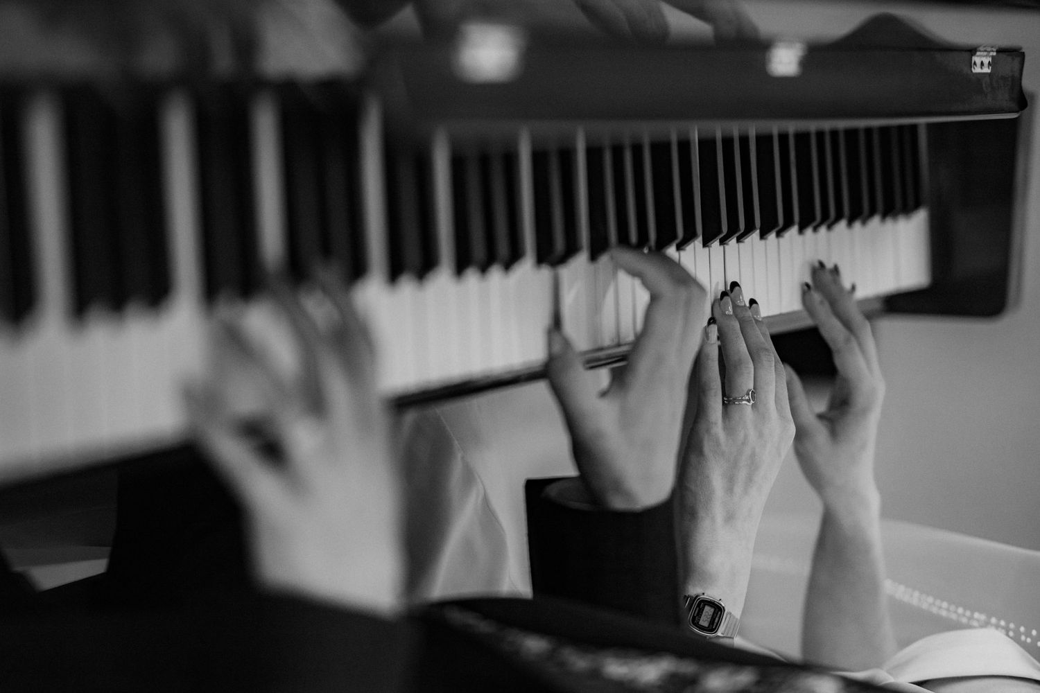 Black and white photo of hands playing piano keys, showcasing elegant finger placement on a keyboard.
