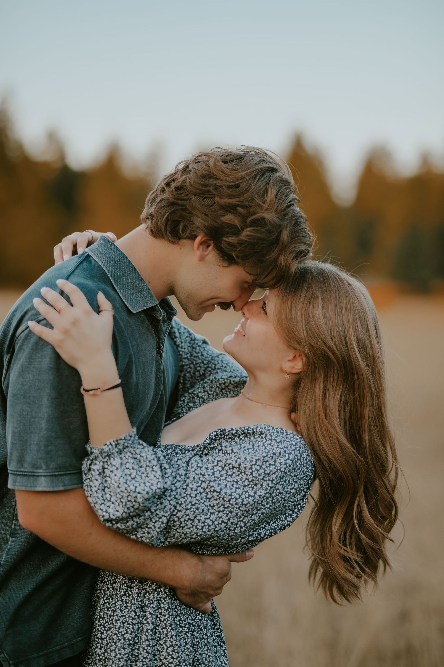 Romantic couple in warm autumn sunset light sharing an intimate embrace in an outdoor field.