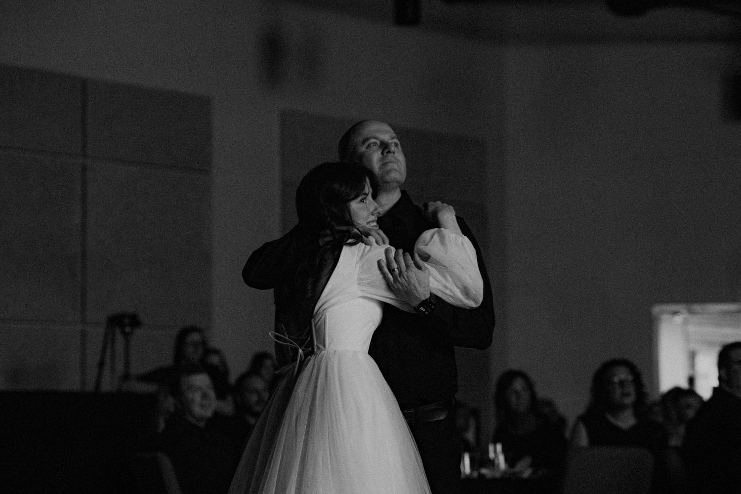 A father & daughter shares an emotional moment together during a wedding reception watching a video in black and white photography.