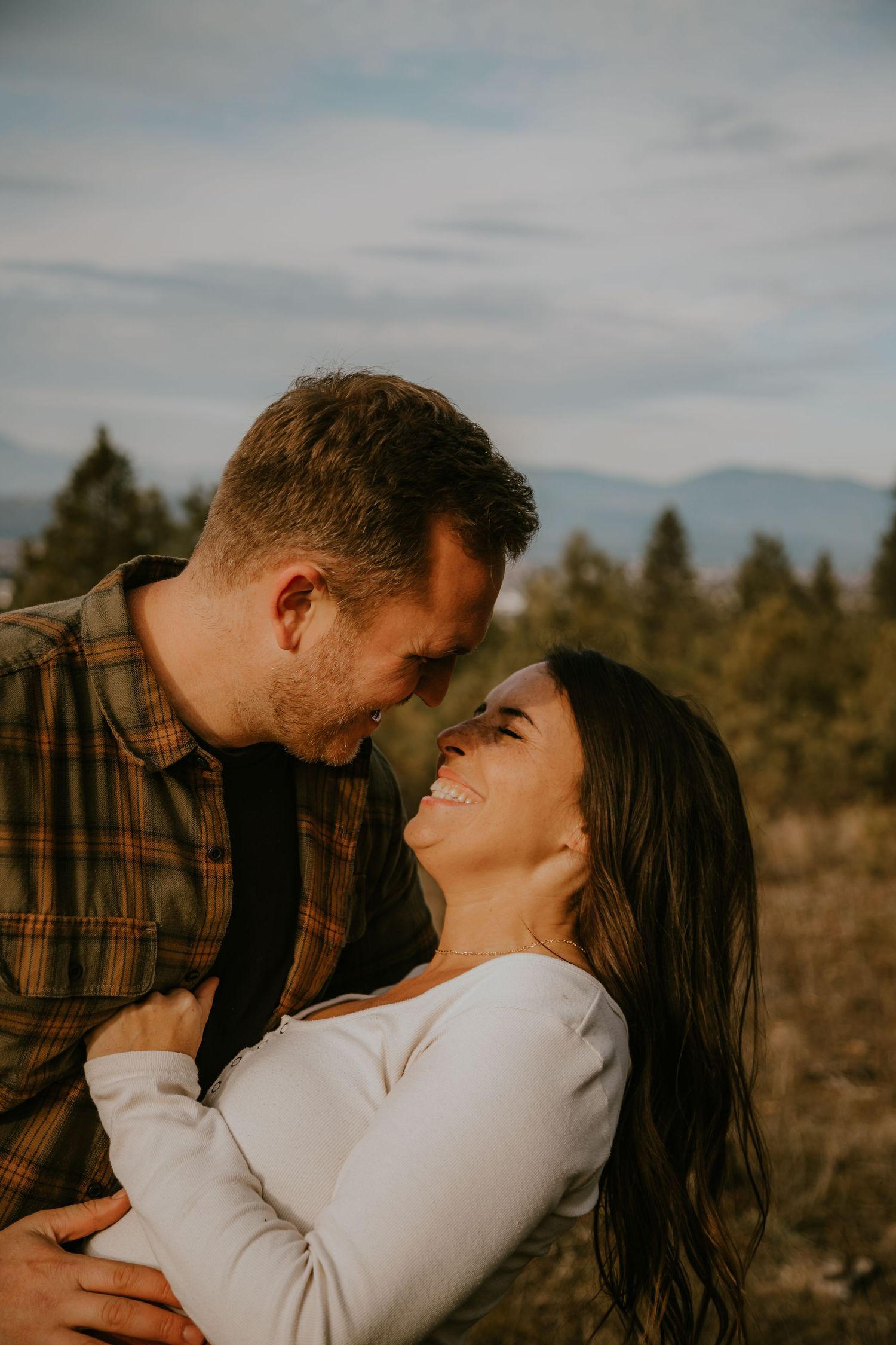 A loving couple share an intimate moment outdoors with mountains and trees in the background at golden hour.
