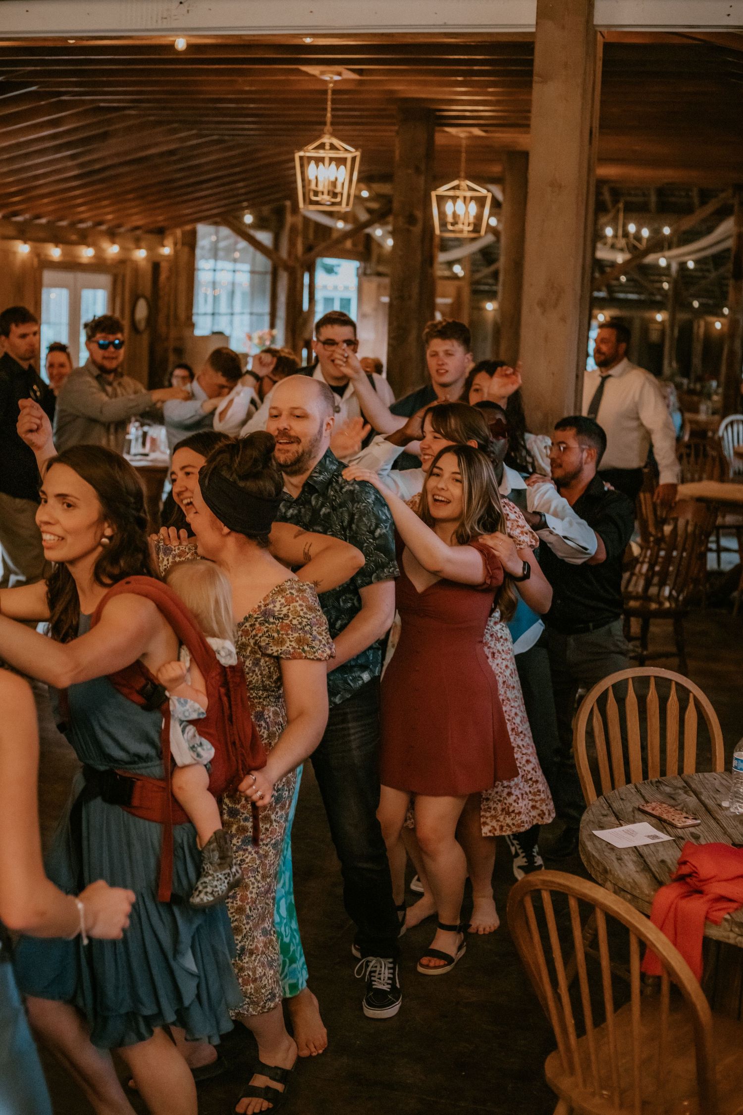 Guests dancing and celebrating at a rustic barn wedding reception with warm string lights and wooden decor.
