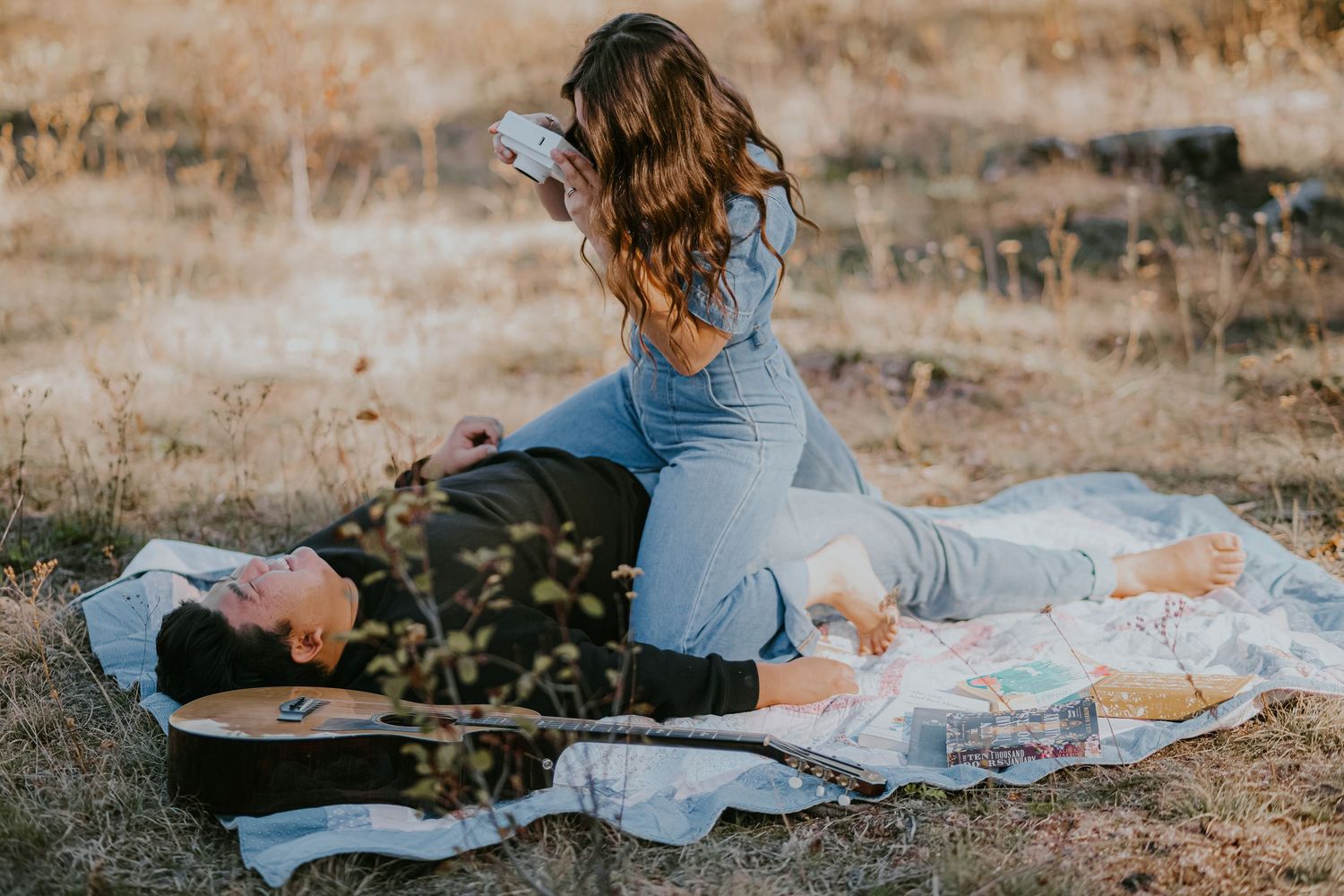 A person in a white dress lies on a blanket reading a book in a rustic outdoor setting during golden hour.