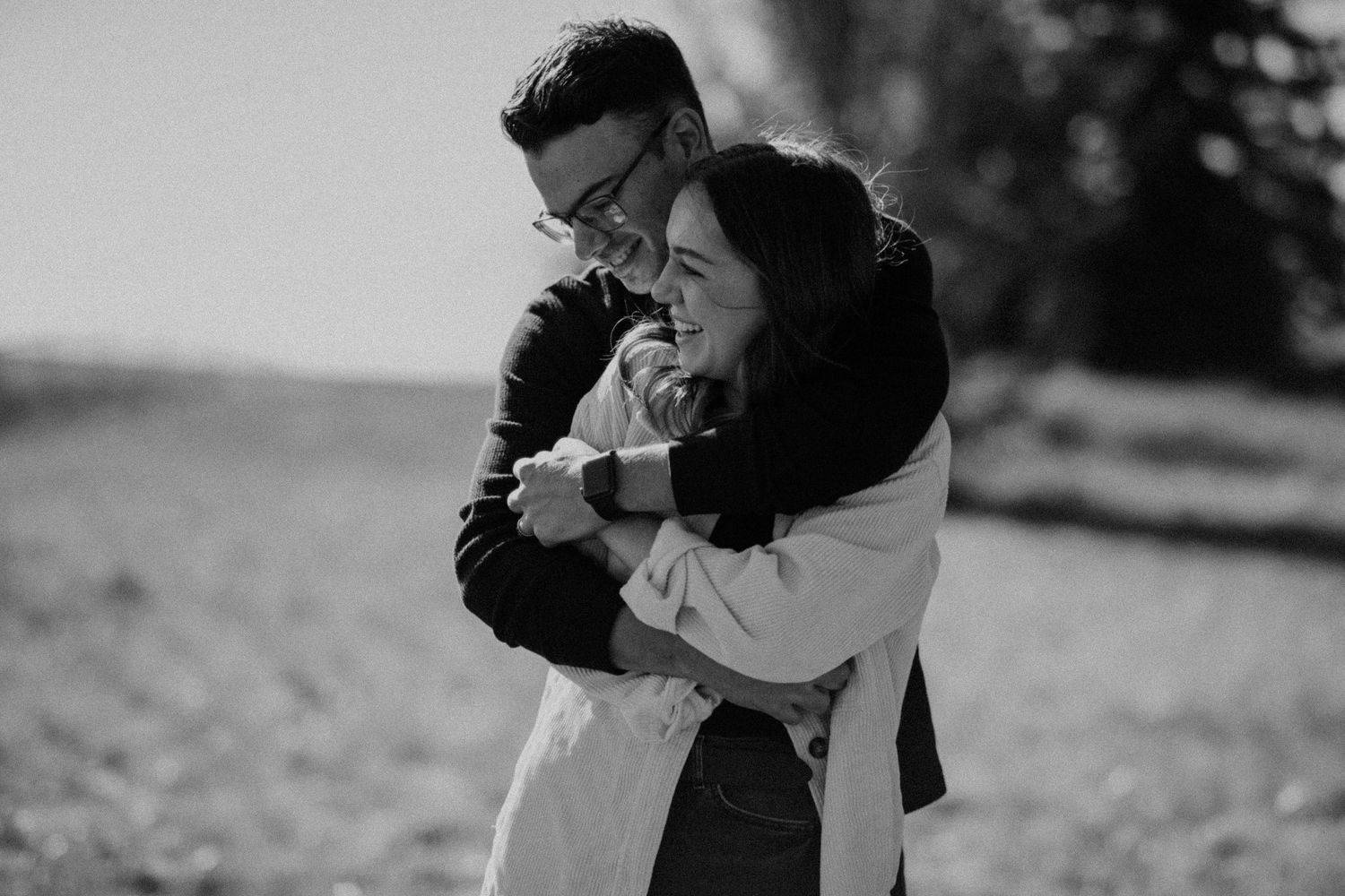 A romantic black and white portrait of a couple embracing outdoors in soft natural lighting.