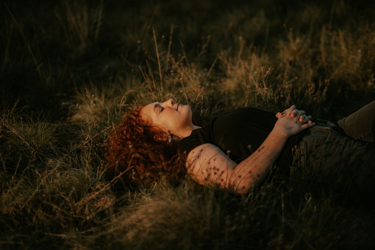 Person lying on autumn ground surrounded by fallen leaves during sunset, creating a dreamy outdoor portrait.