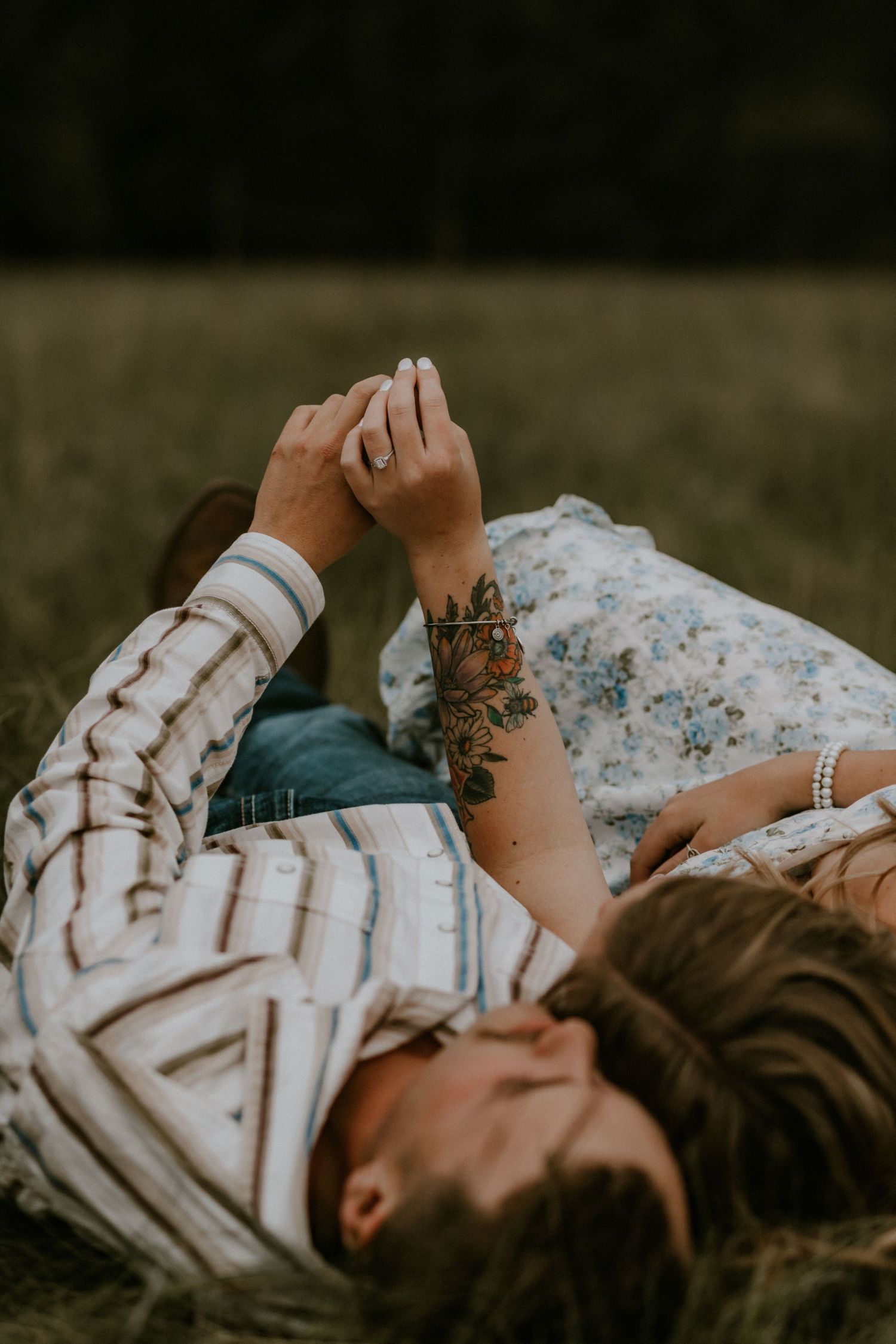 Person lying in grass wearing a white patterned sweater and floral skirt with visible floral tattoo on arm.