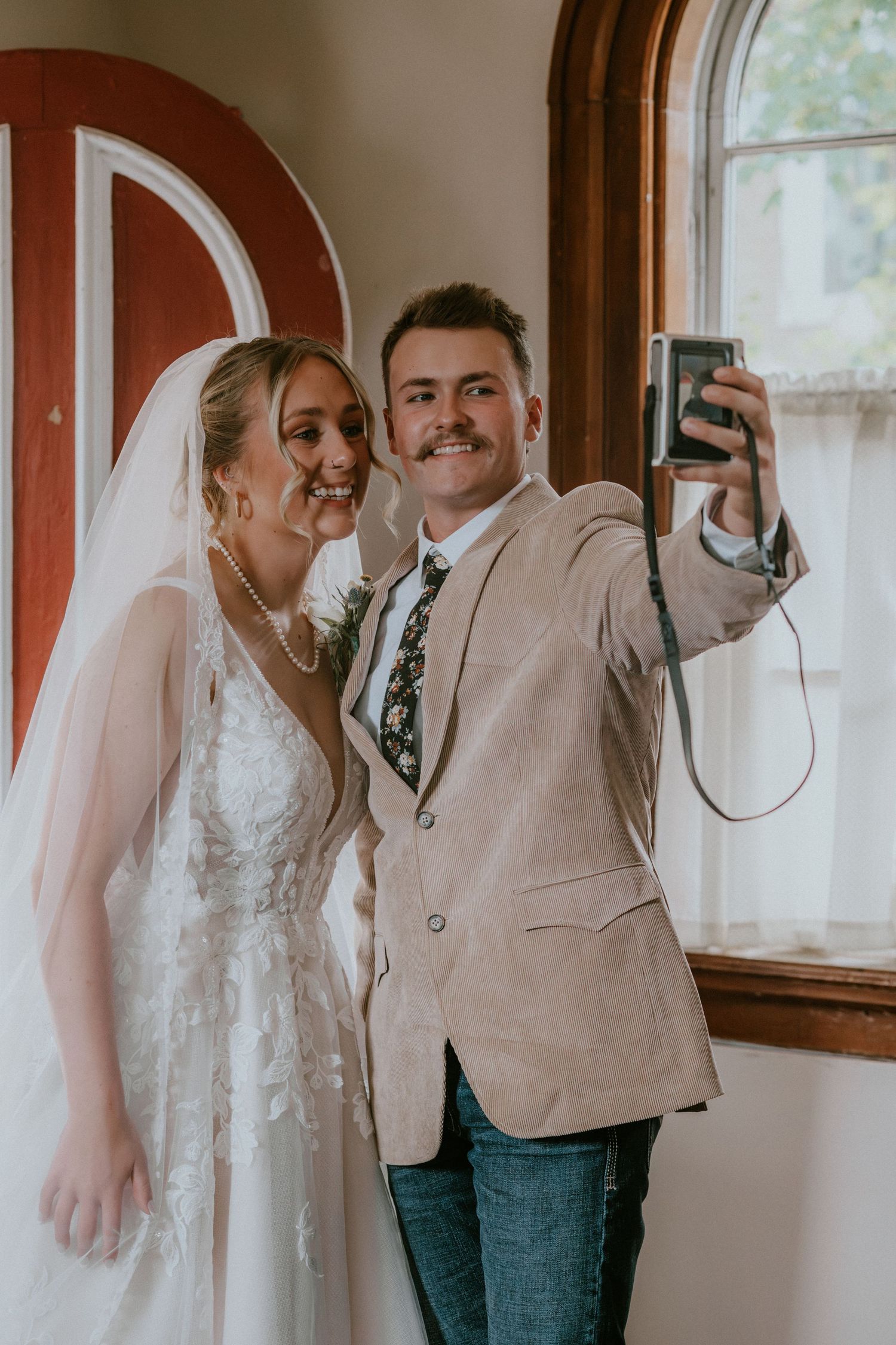 A wedding party in casual attire including jeans and vests poses together in a rustic indoor setting.