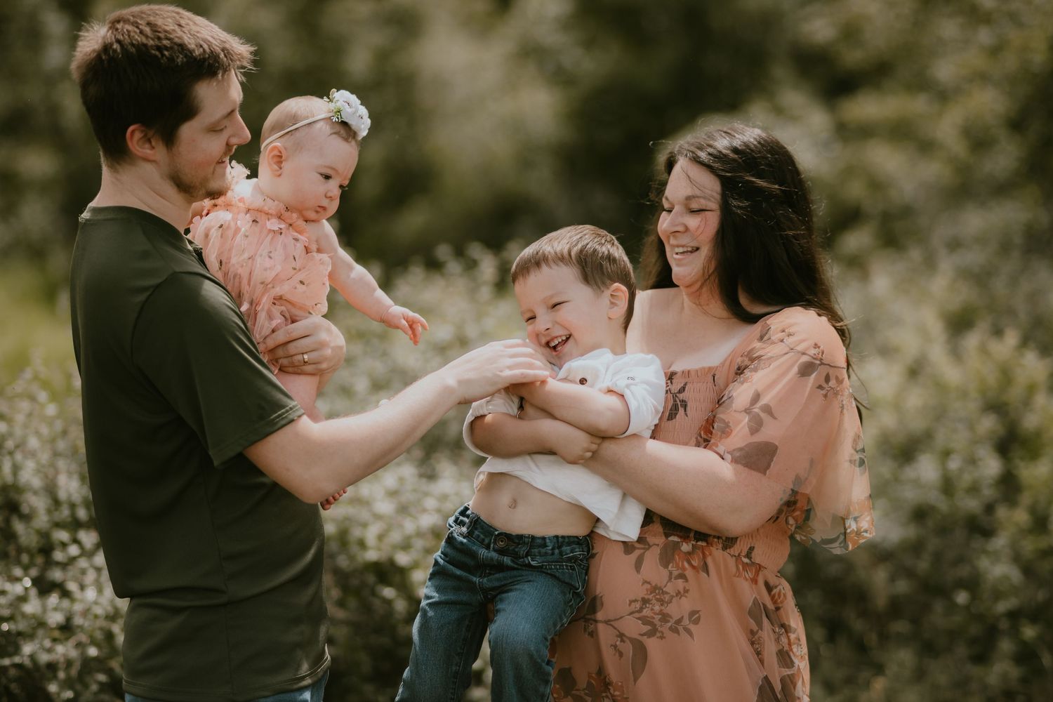 A family shares a joyful moment together outdoors in a natural setting with soft lighting and greenery.