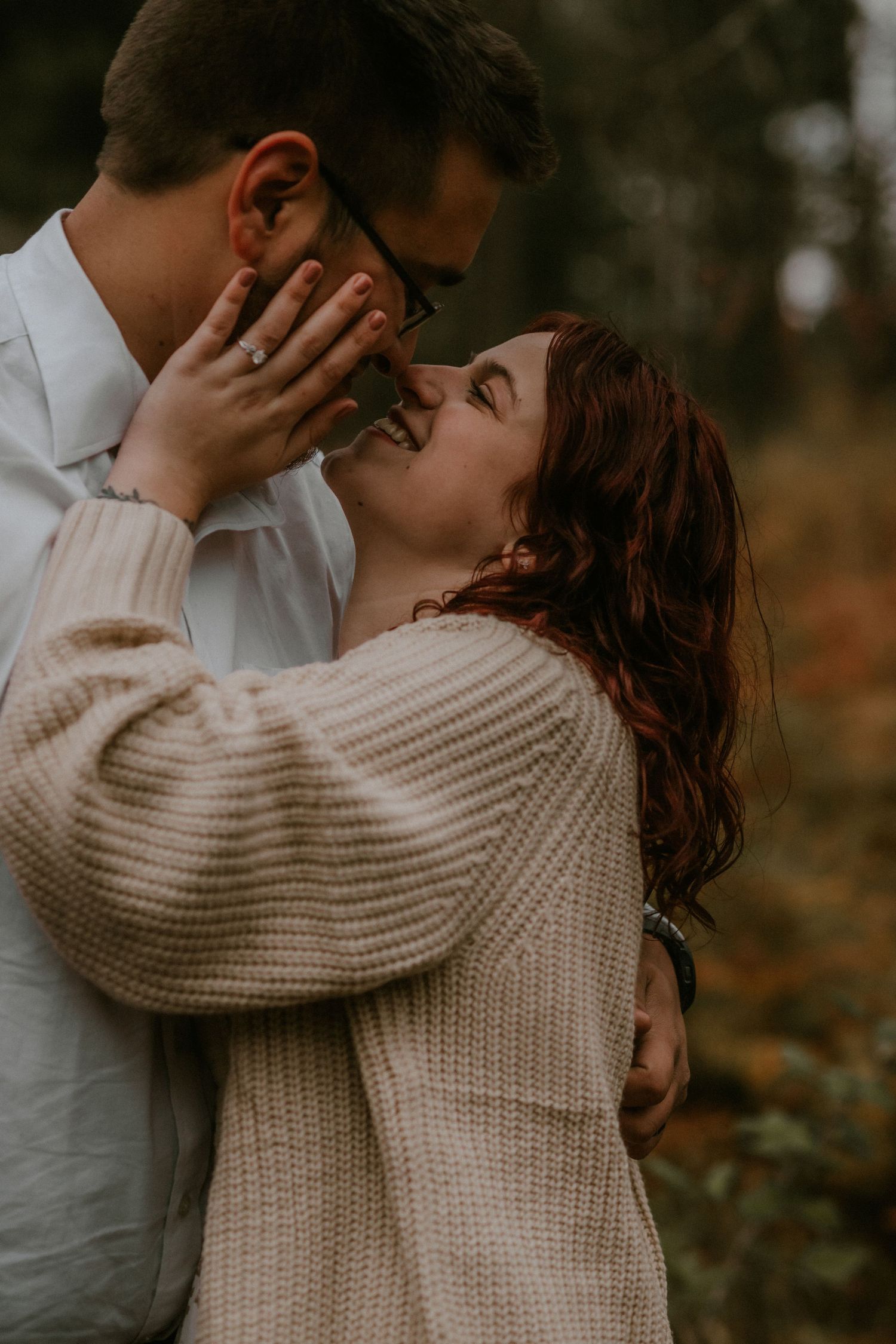 A romantic couple embraces outdoors while wearing cozy sweaters in an autumn setting.