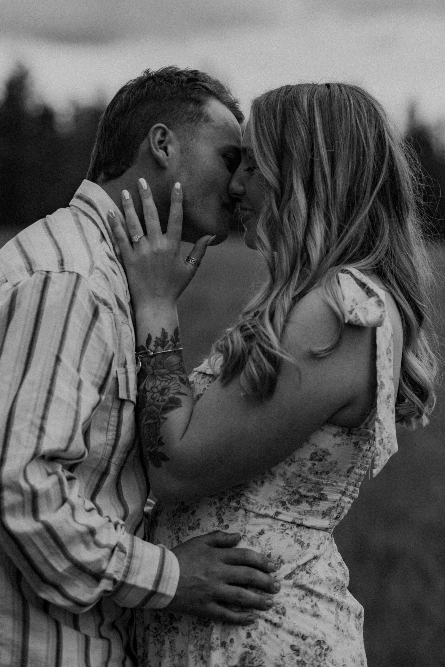 A romantic black and white photo shows a couple in an intimate embrace, sharing a tender moment outdoors.