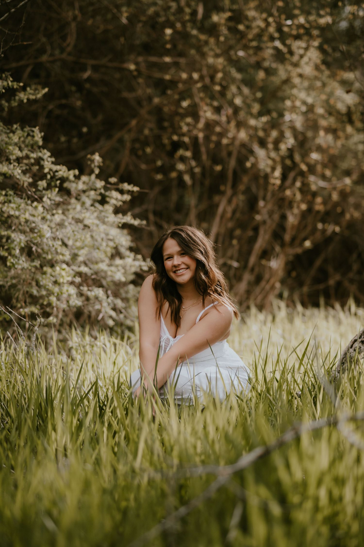 A person sits in tall grass with white wildflowers blooming in a natural outdoor setting.
