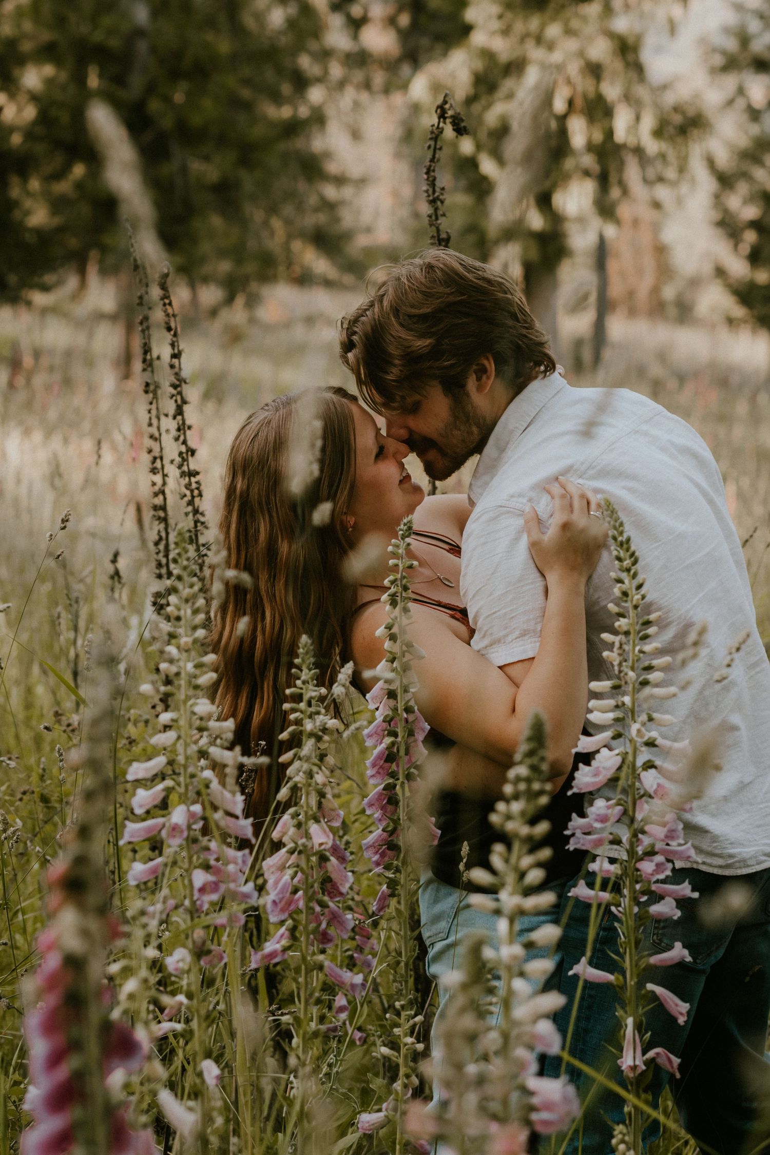 A romantic couple embraces in a field of tall purple wildflowers during golden hour.