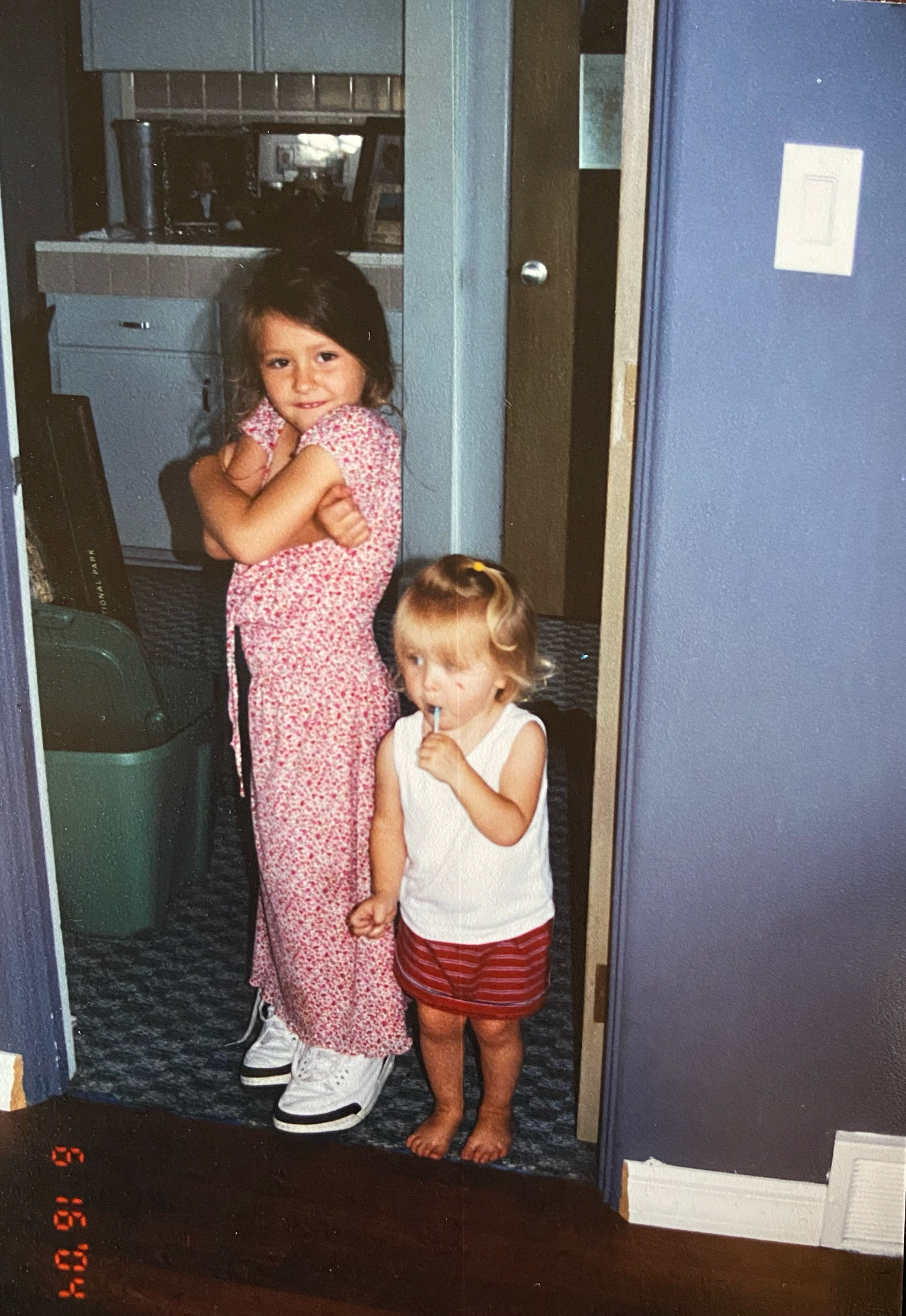 Two young children stand together in a home doorway wearing casual clothes on a summer day.