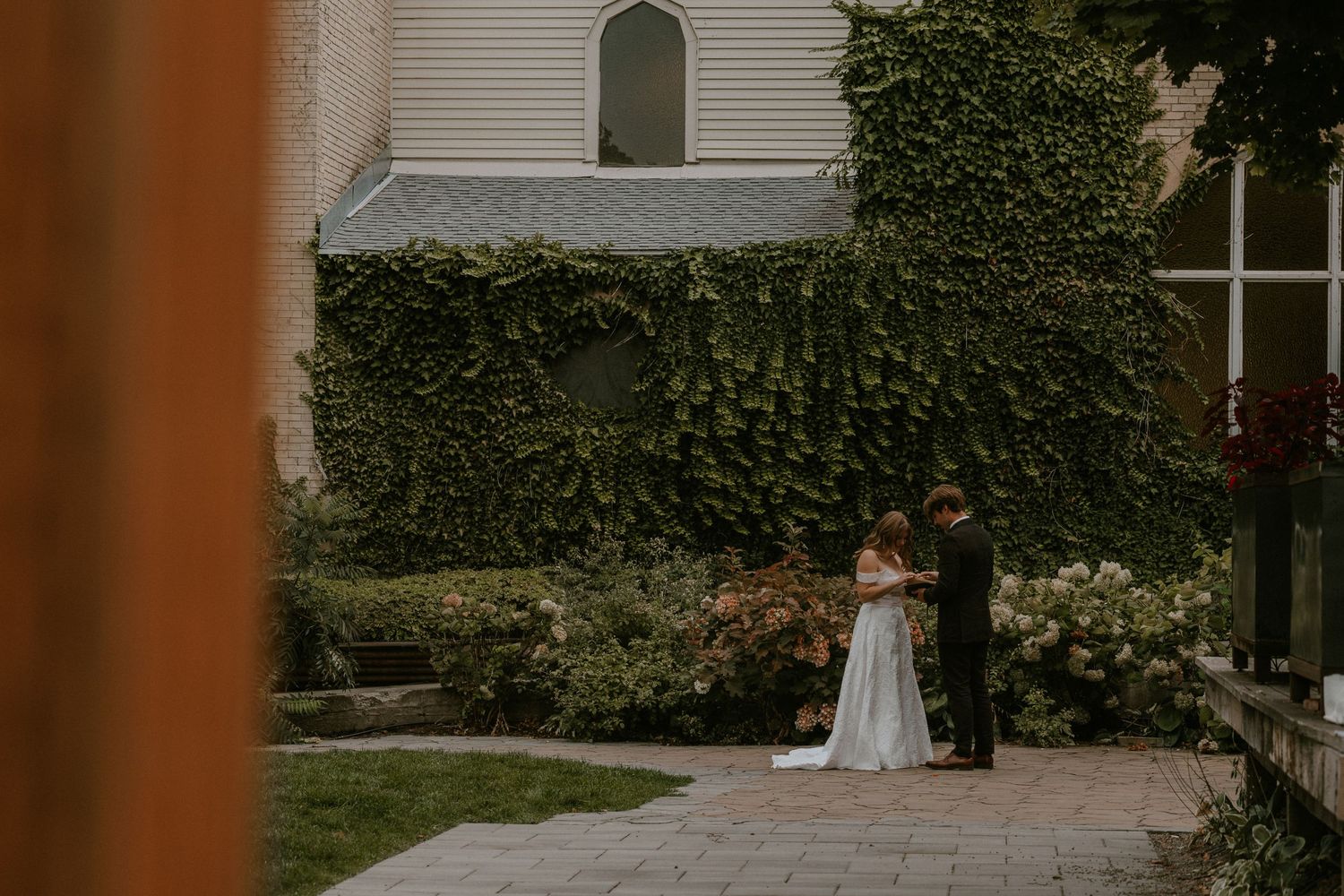 Bride and groom share a romantic moment in a lush ivy-covered garden courtyard during their outdoor wedding ceremony.