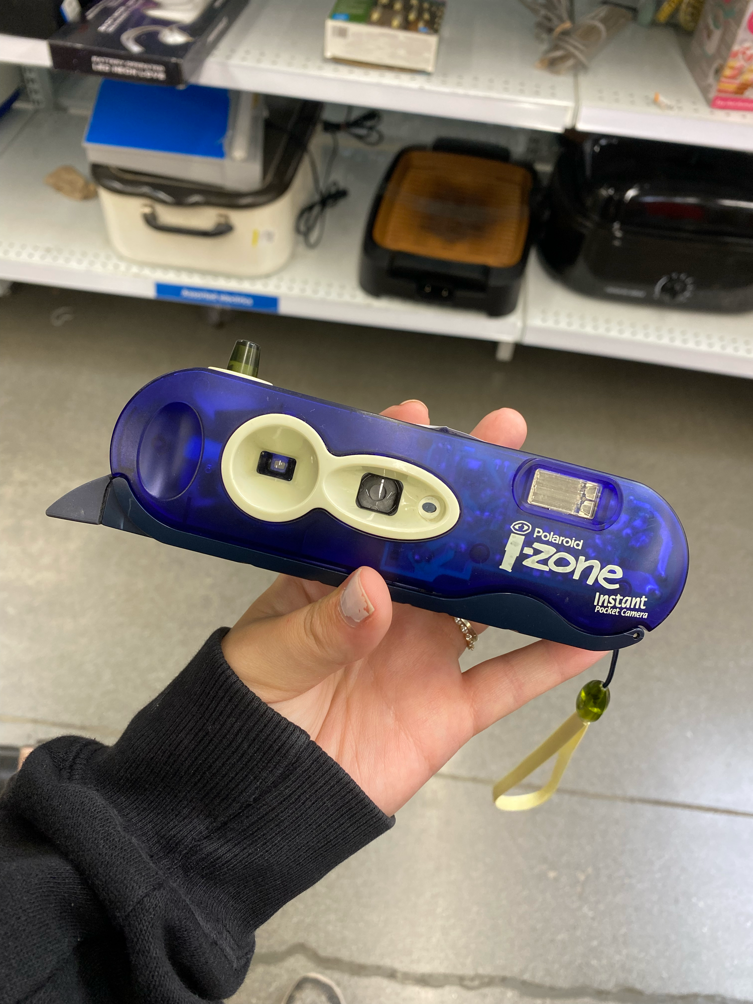 Hand holding a blue digital thermometer with LCD display showing temperature reading in a clinical setting.