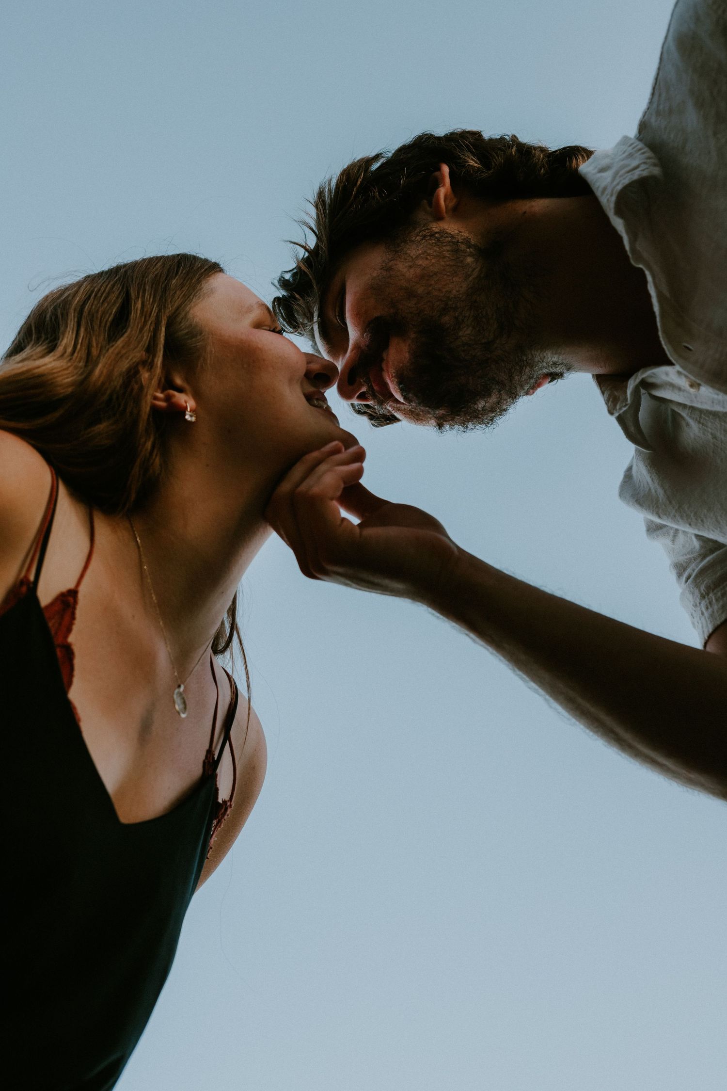An intimate close-up artistic photo of a romantic couple about to kiss against a light blue sky background.