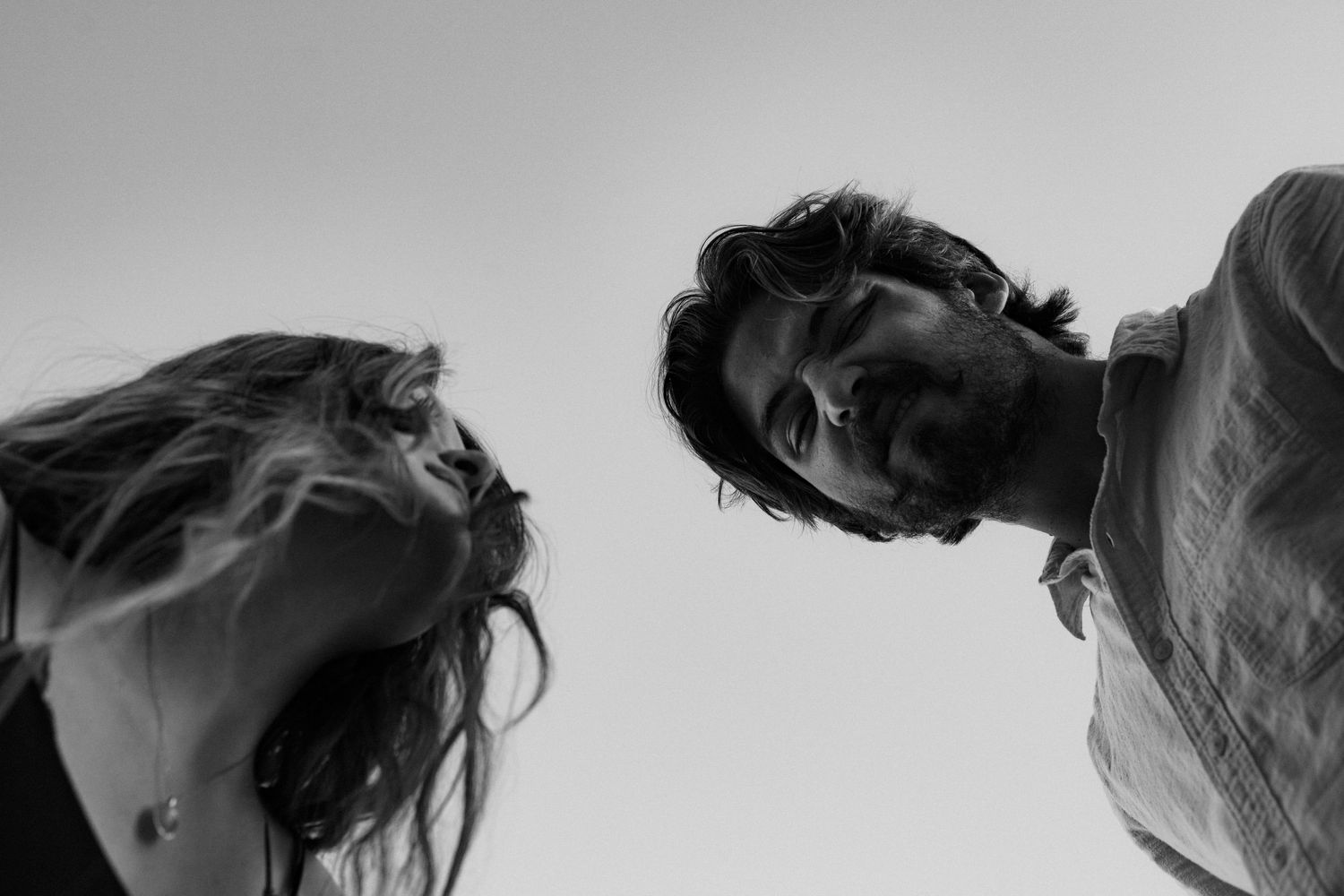 A dramatic black and white low angle shot of two figures looking down at the camera.