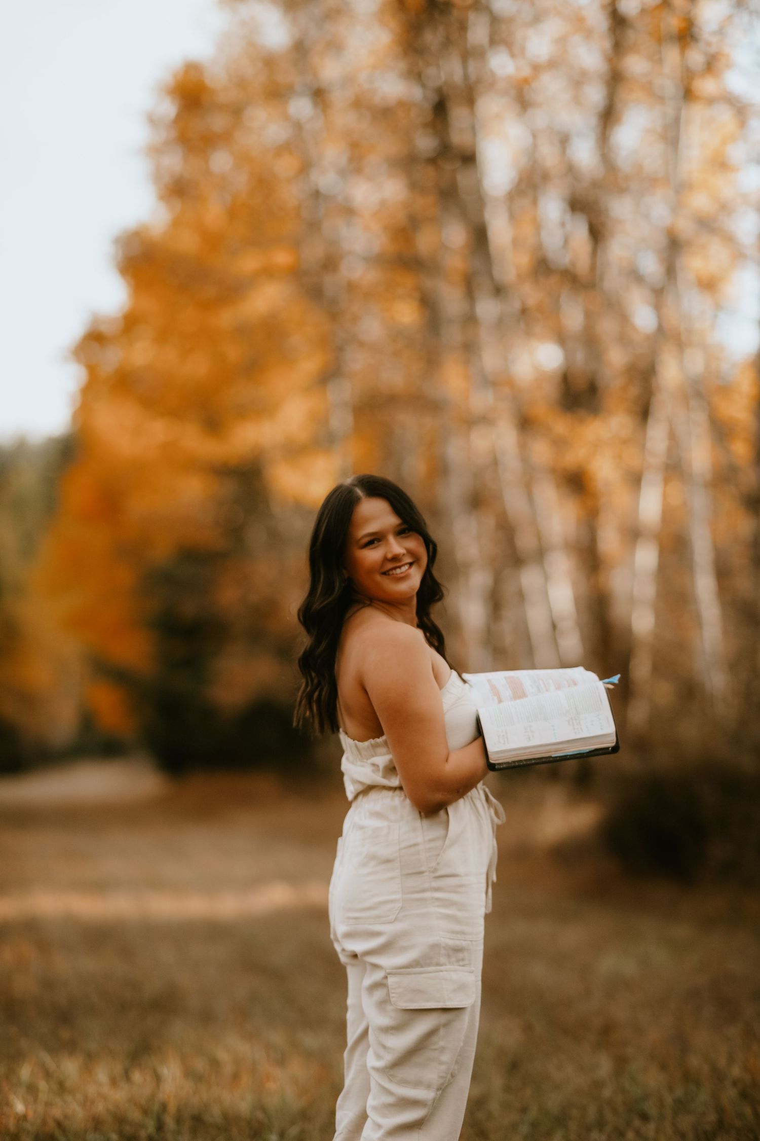 Woman in white dress spins joyfully in a golden autumn field with birch trees in the background.